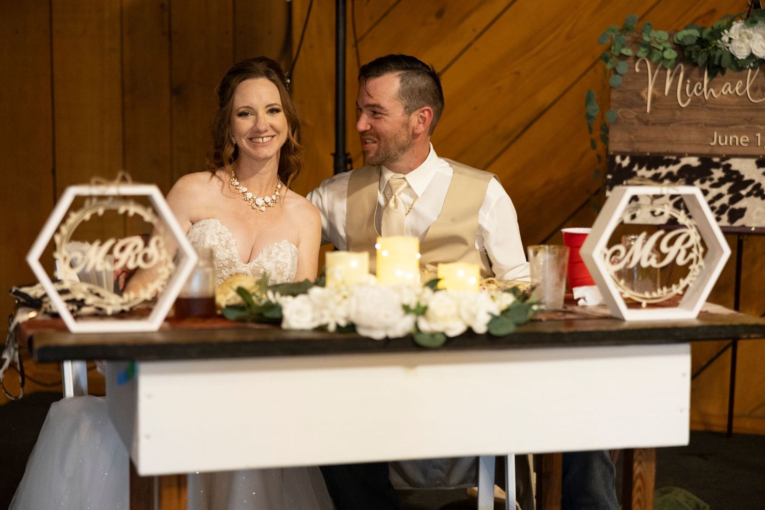 Wedding reception decor features illuminated hexagonal signs and white floral arrangements on a wooden shelf display.