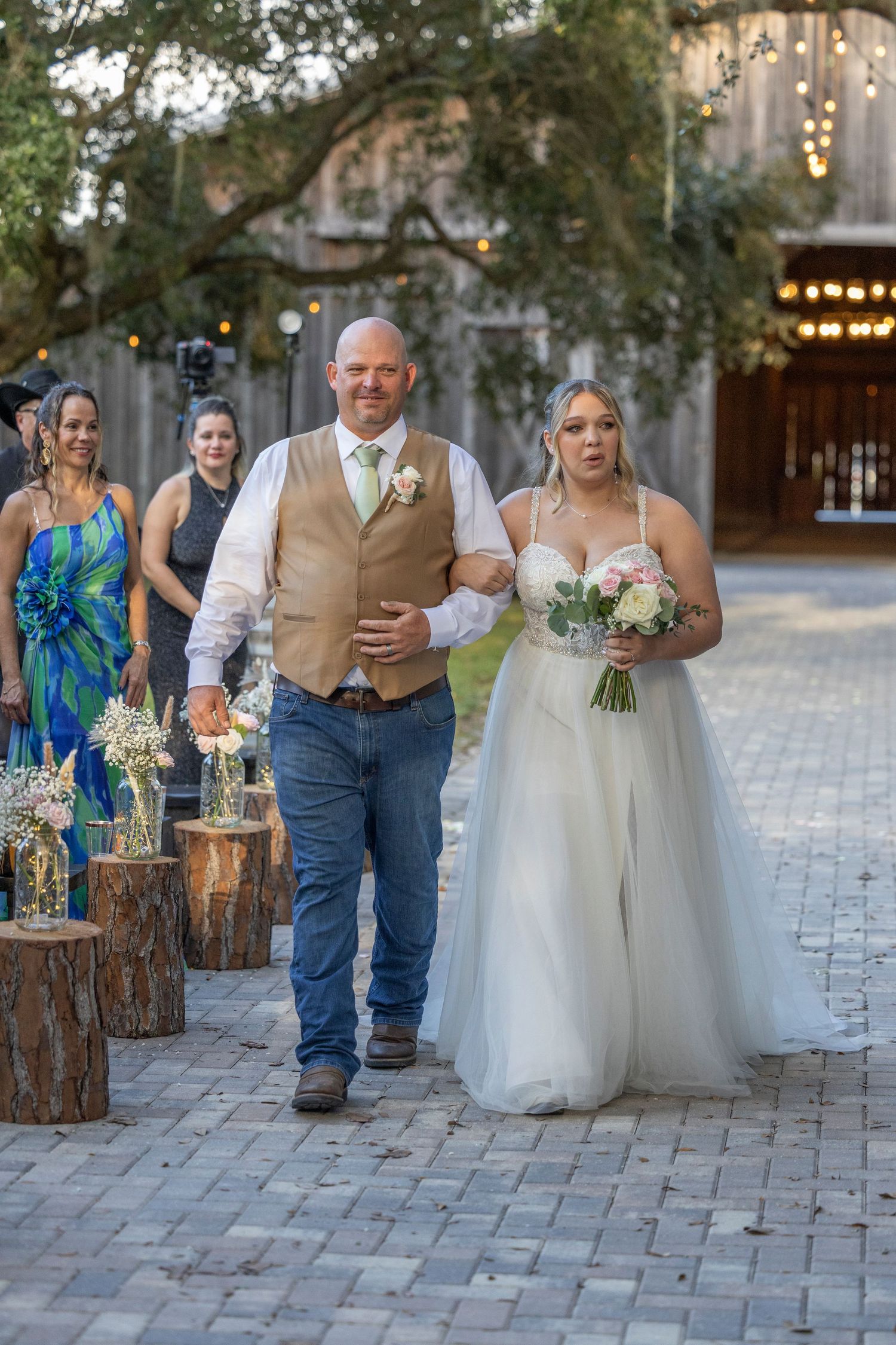 A couple poses together on a rustic brick patio with wooden log decor and twinkling lights at an outdoor wedding venue.