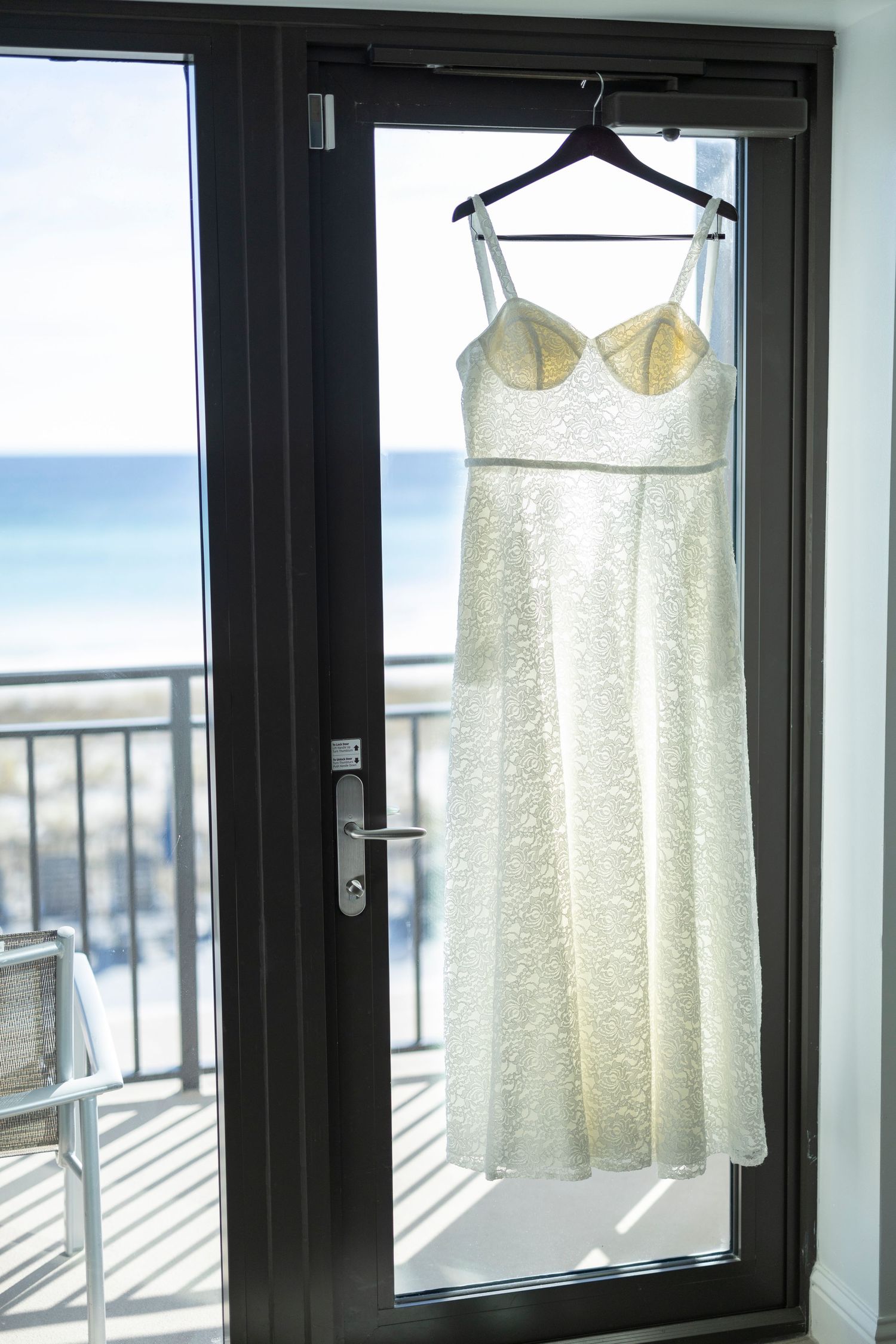 A white lace dress hangs by a window overlooking a city skyline, creating a dreamy silhouette against natural light.