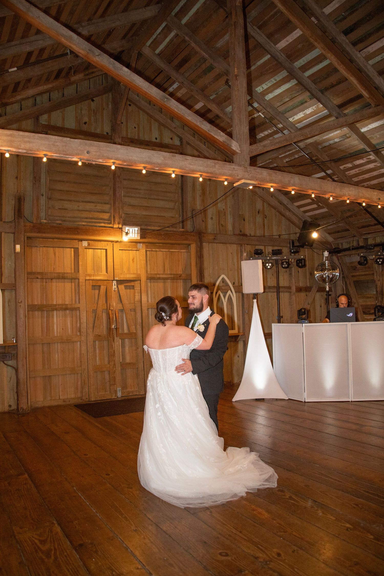 A rustic barn venue with wooden beams and twinkling lights creates a romantic atmosphere for a wedding celebration.