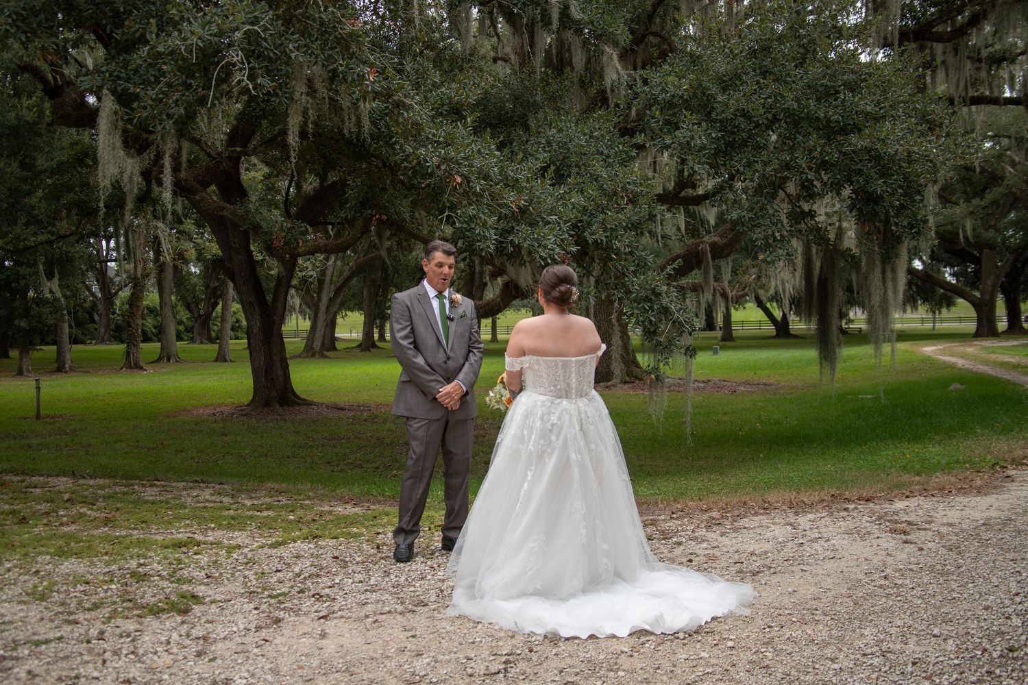 A couple in wedding attire walks along a tree-lined path during their outdoor photo session.