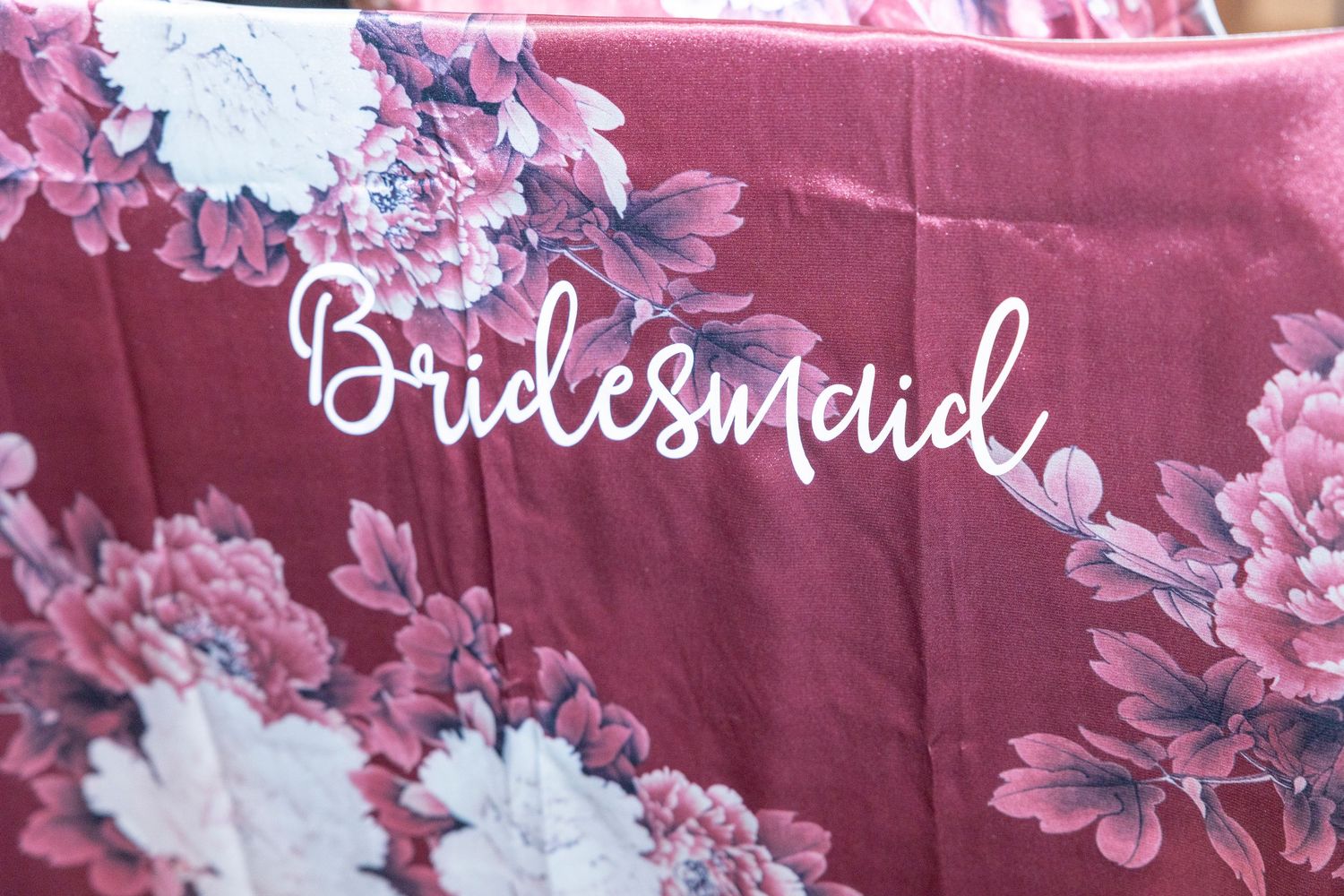 Pink floral bridesmaid robe with decorative white script lettering and delicate flower pattern.