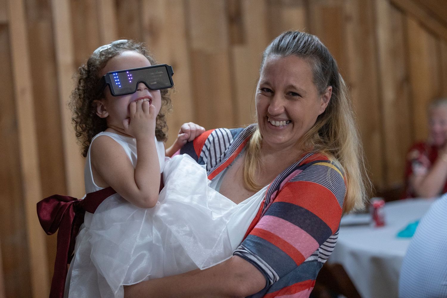 Mother and child share playful moment during wedding reception in rustic venue setting.