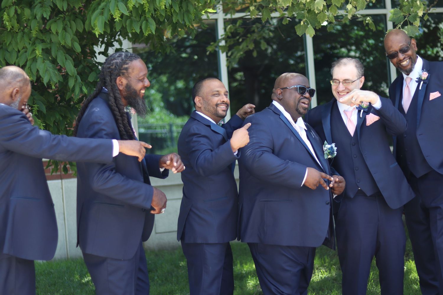 A group of groomsmen in navy blue suits laughing and celebrating outdoors at a wedding ceremony.