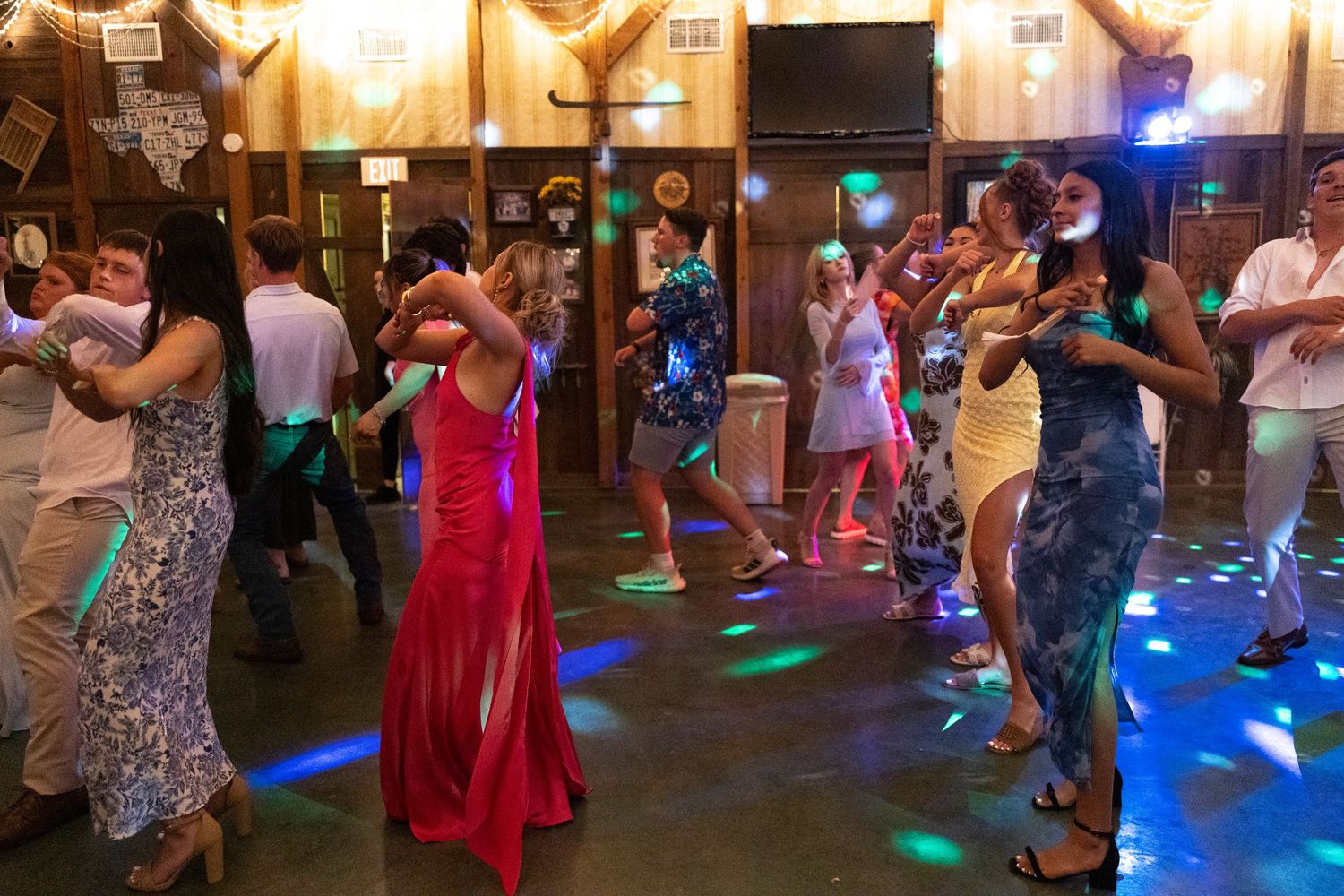 Couples dancing in formal attire under colorful disco lights at an indoor dance event or prom.