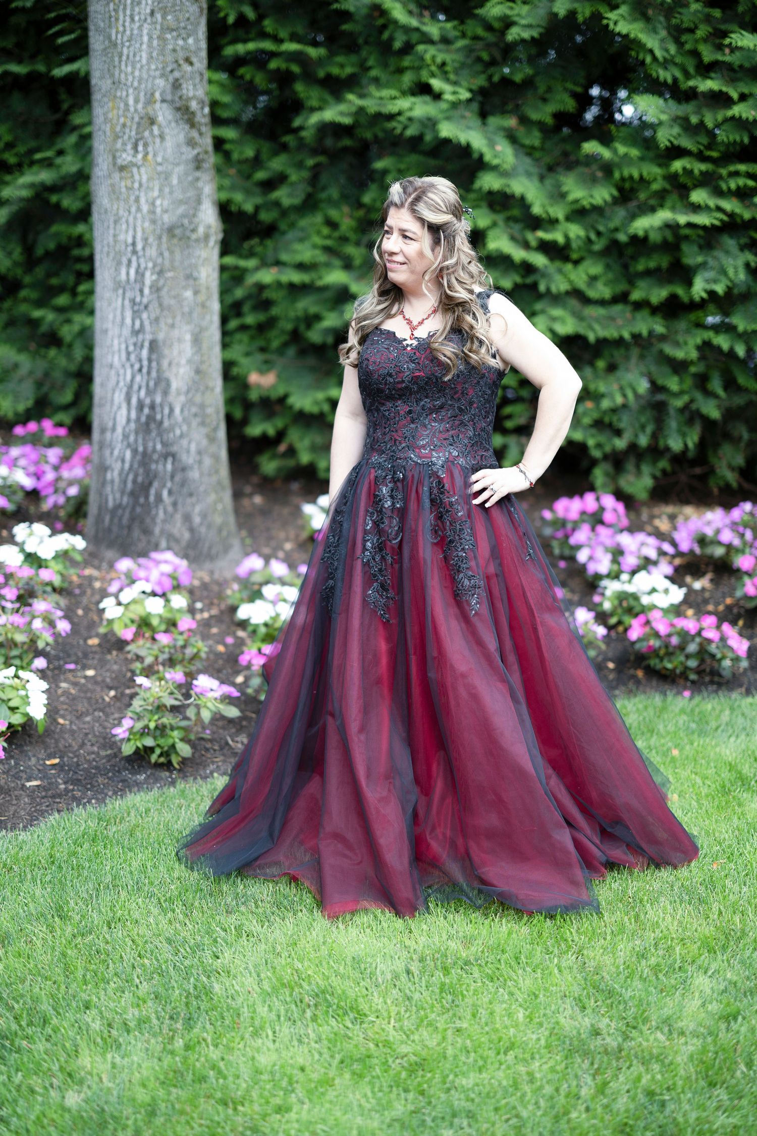 A flowing burgundy and black tulle gown with lace bodice photographed in a garden setting with blooming flowers.