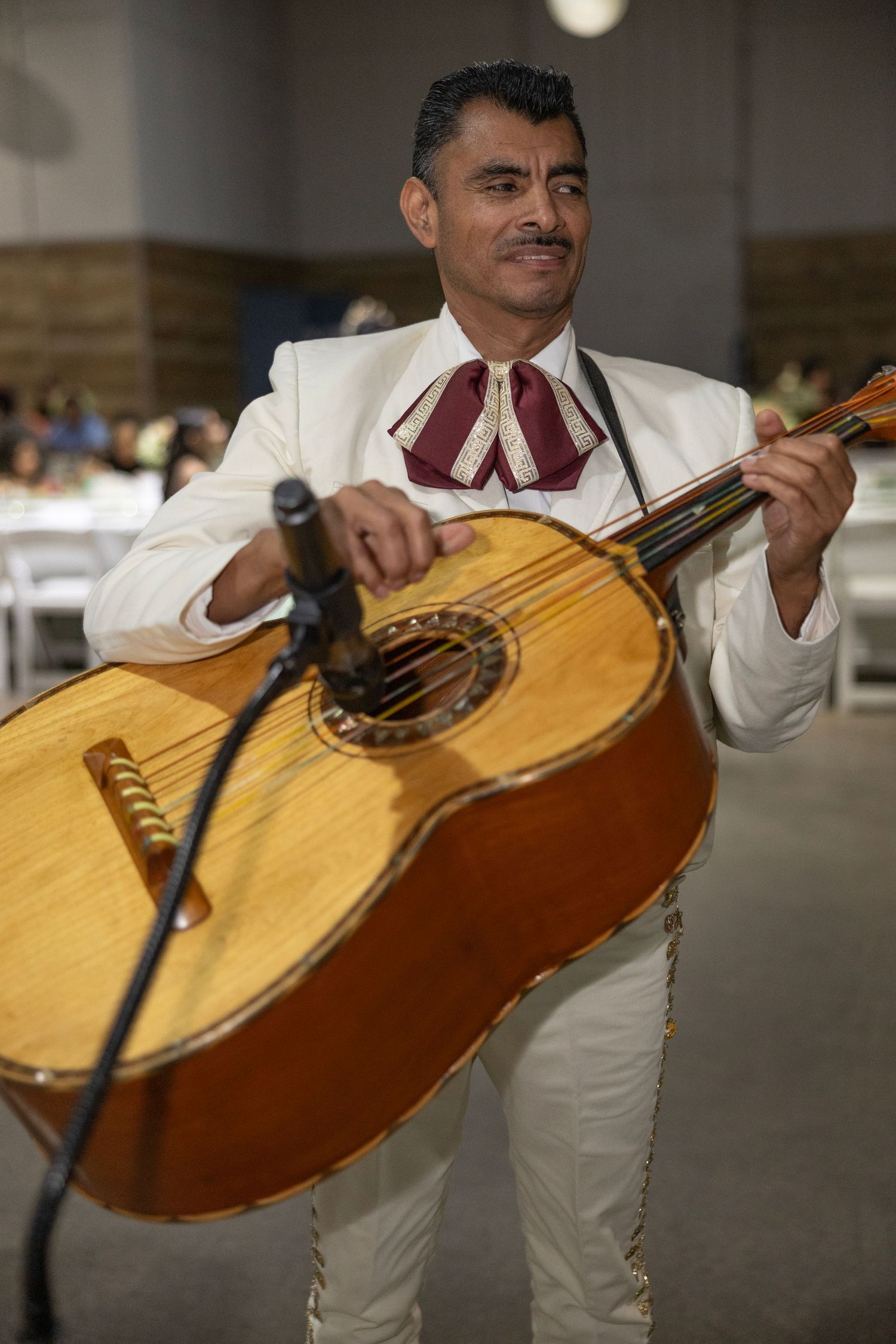 A musician in white attire plays a large traditional Mexican guitarron instrument during a performance.