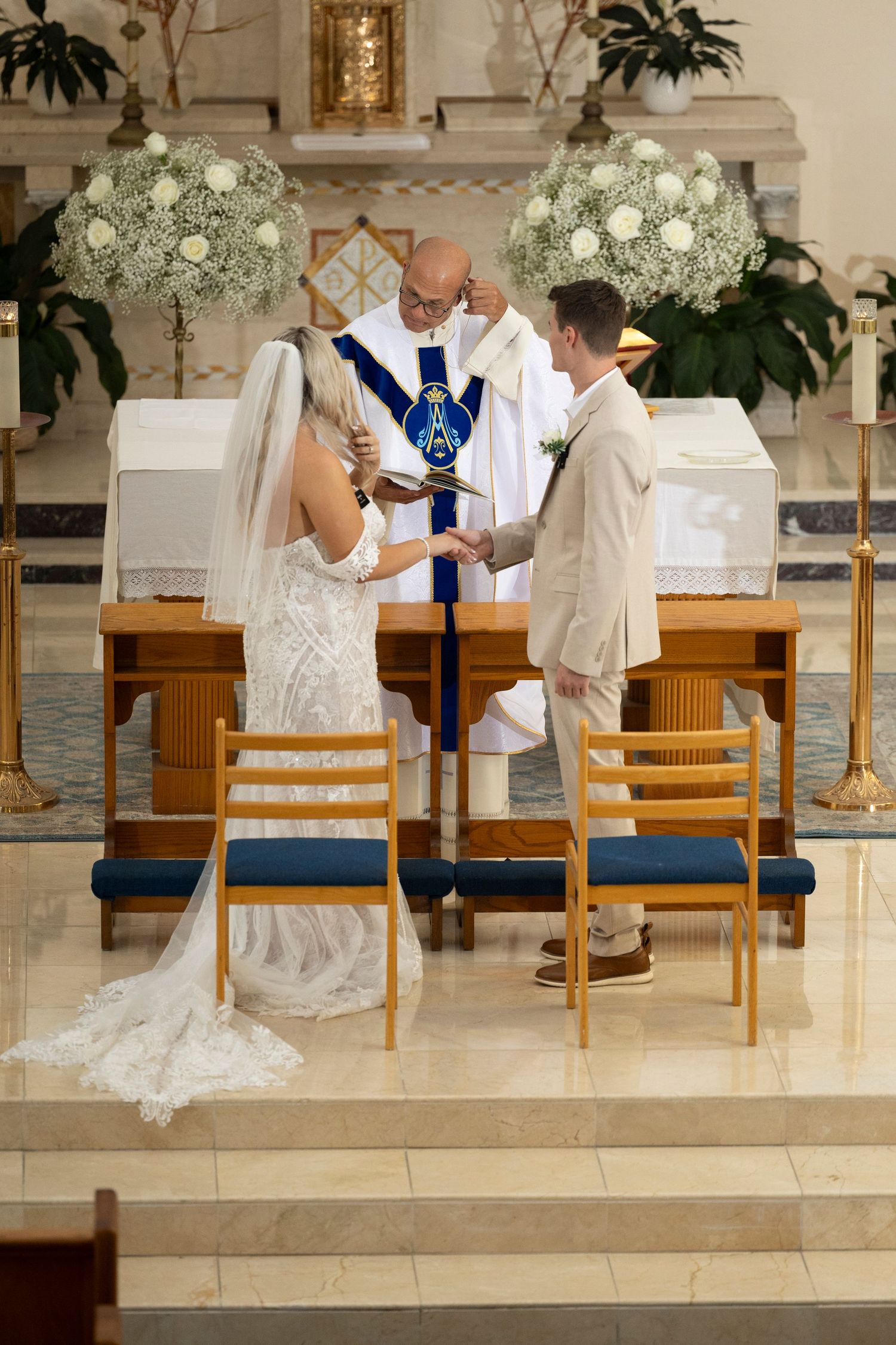 A couple sits together during a wedding ceremony in a church with white floral decorations and wooden pews.