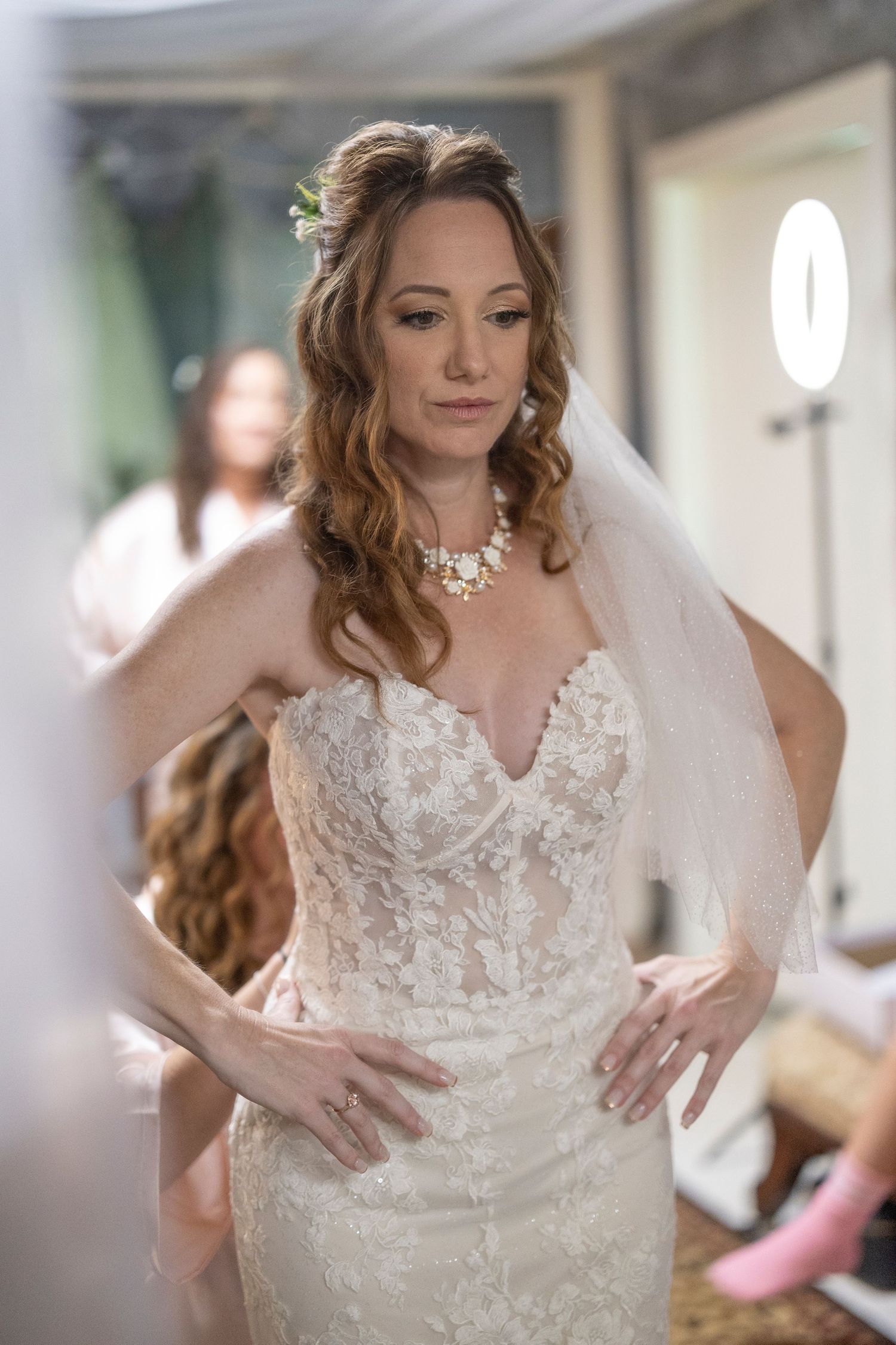 A bride in a white lace wedding dress shows off intricate details during her final fitting preparations.