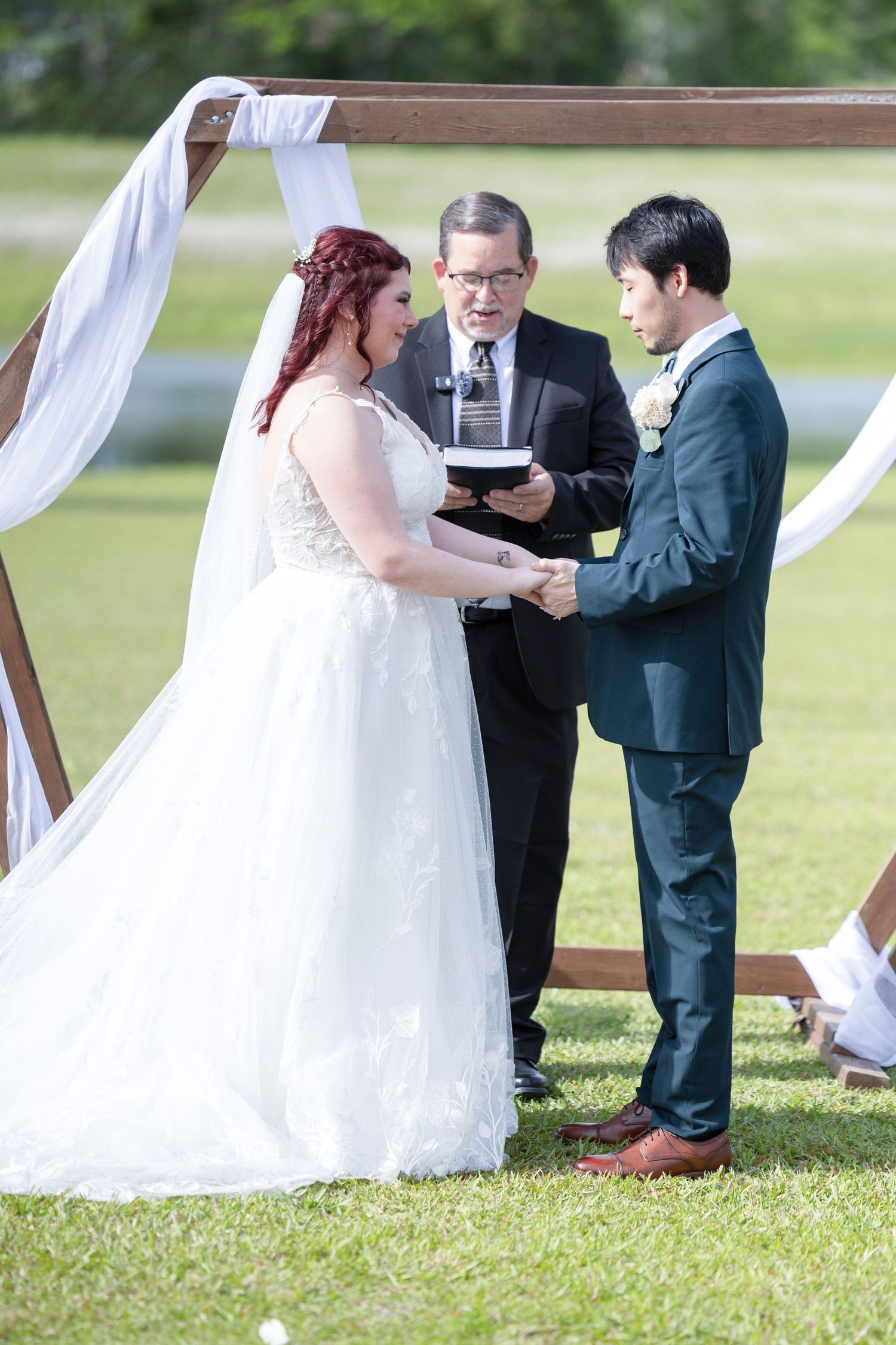 Outdoor wedding ceremony with white fabric draping and couple exchanging vows on grassy lawn.