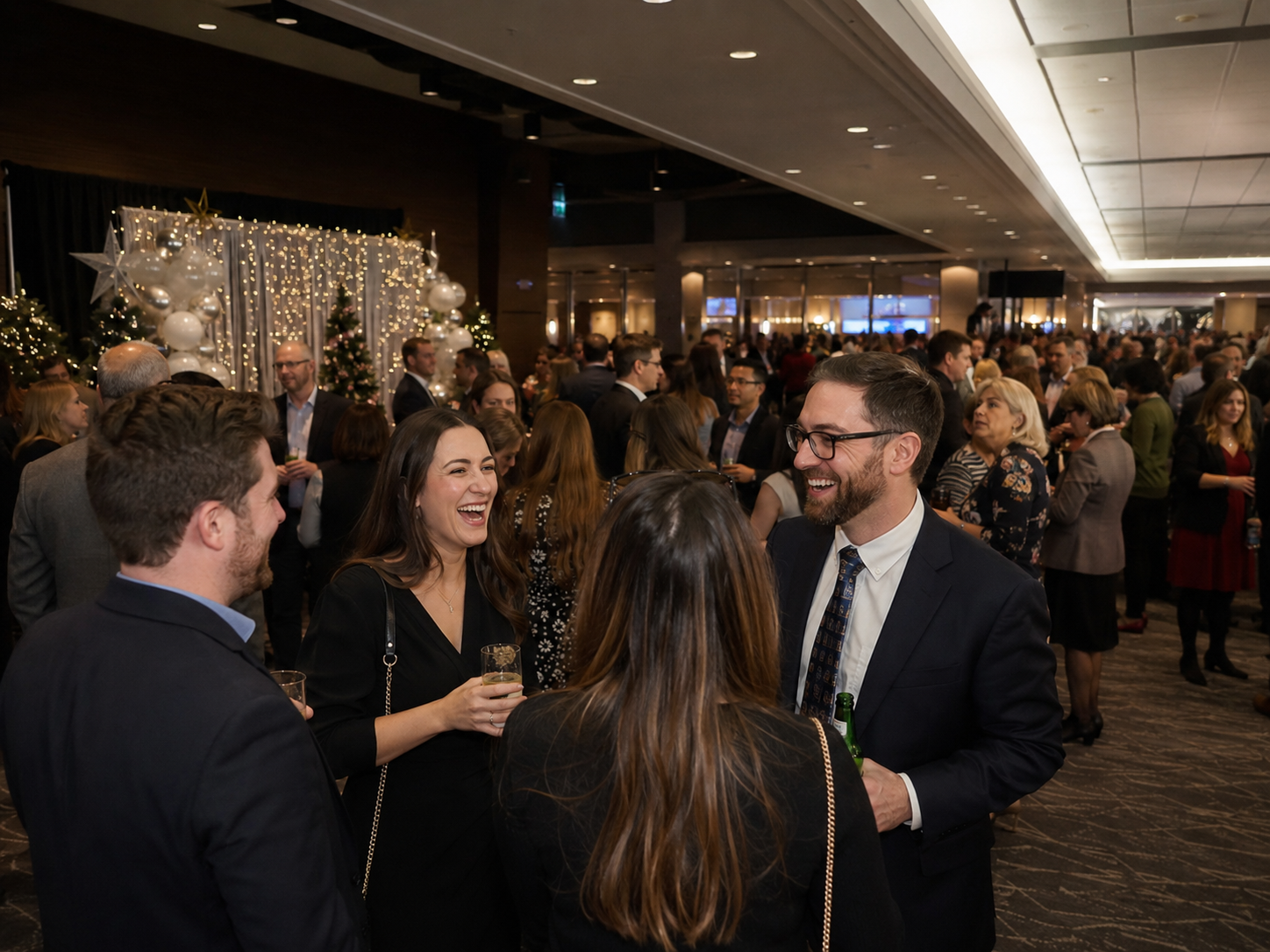 Professionals socializing and laughing at a festive holiday corporate networking event with Christmas decor.