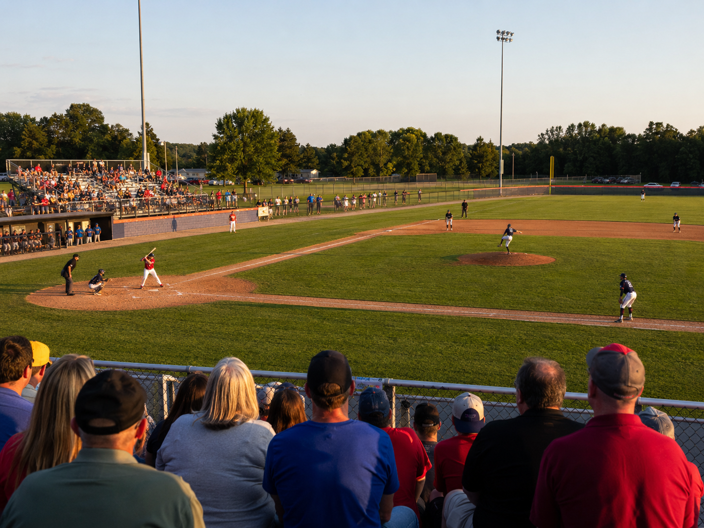 Fans watch a summer evening minor league baseball game at a well-lit community ballpark.