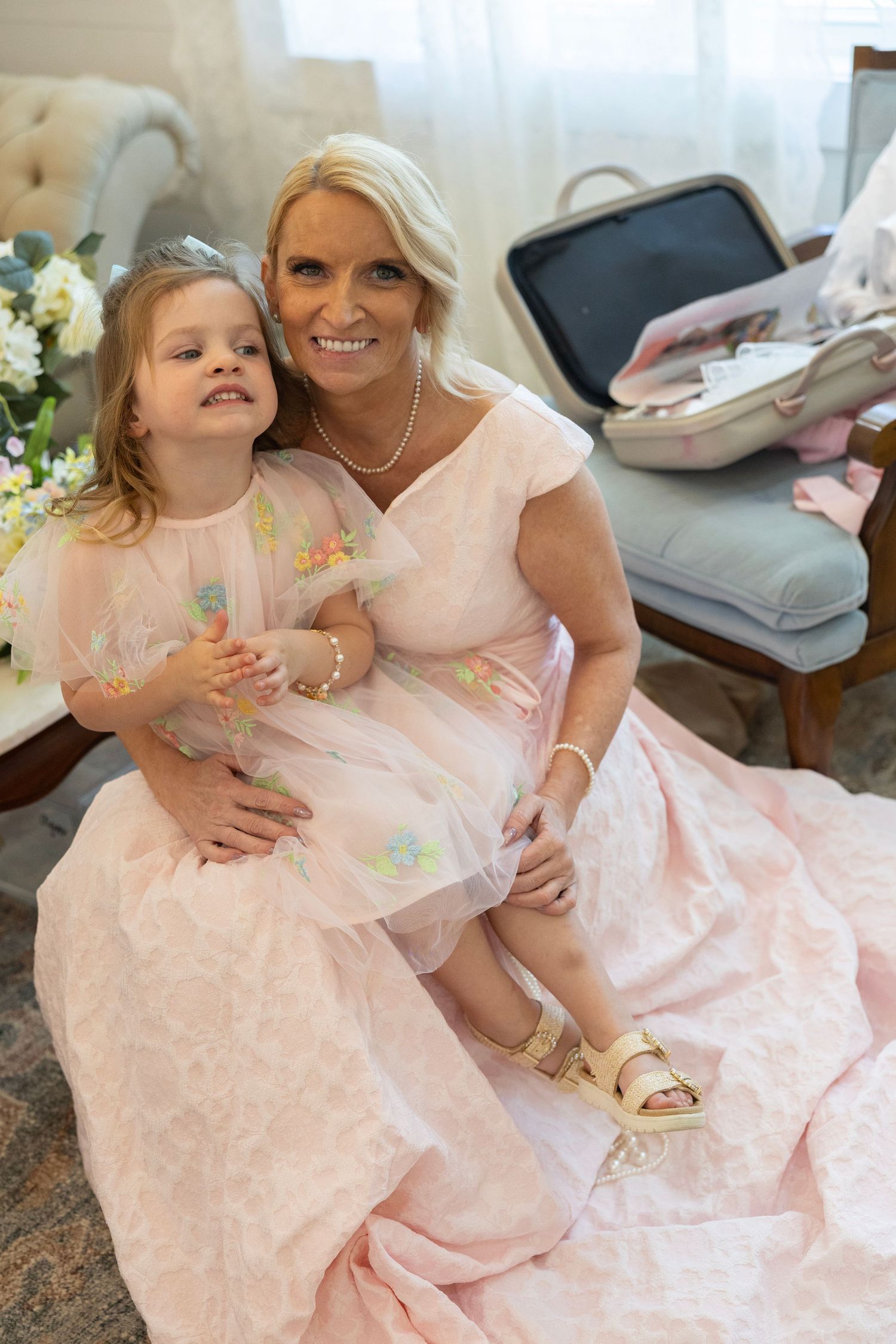 Woman and young girl in matching pink dresses sitting together, smiling for a portrait in an elegant room.