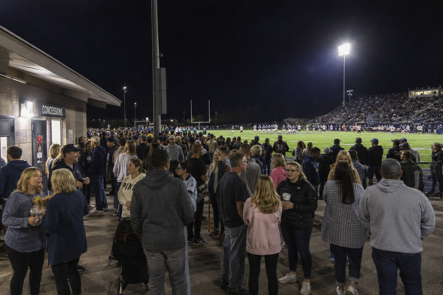 Large crowd gathers at an outdoor stadium under bright lights during a nighttime sporting event.