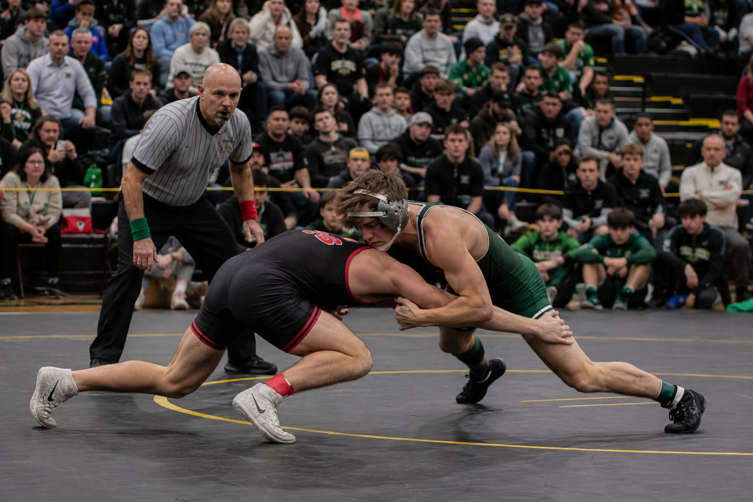 Two wrestlers compete on mat as referee watches during intense high school wrestling match.