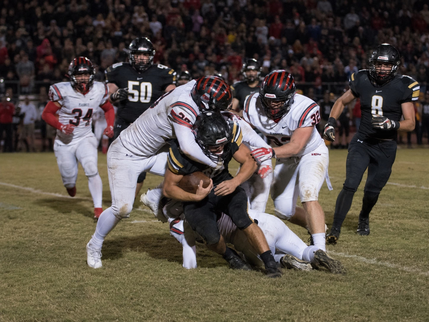High school football player tackled by multiple red jersey defenders during a night game.