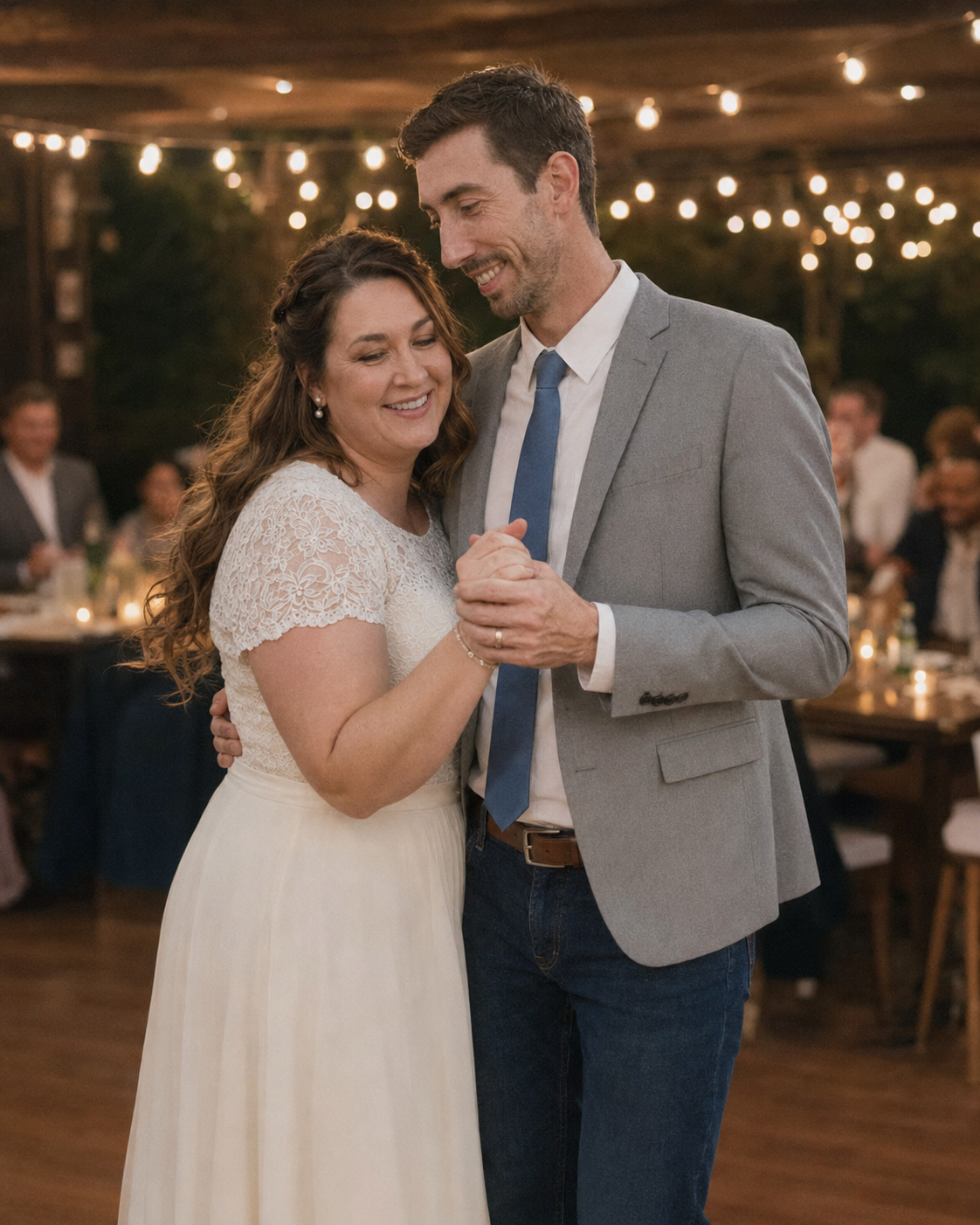 Bride and groom share first dance at romantic barn wedding reception with string lights glowing overhead.