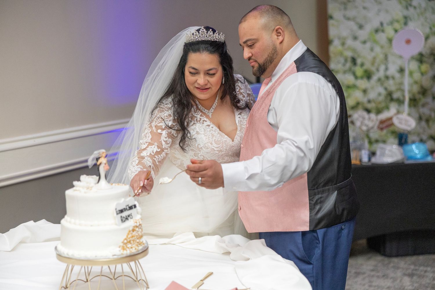Bride and groom cutting their white wedding cake together at their elegant indoor wedding reception celebration.