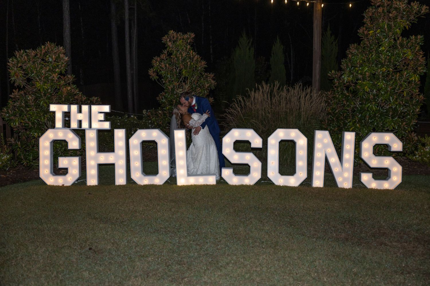Large illuminated letters spelling 'THE CHOLSONS' glow against a dark outdoor backdrop with trees and string lights.