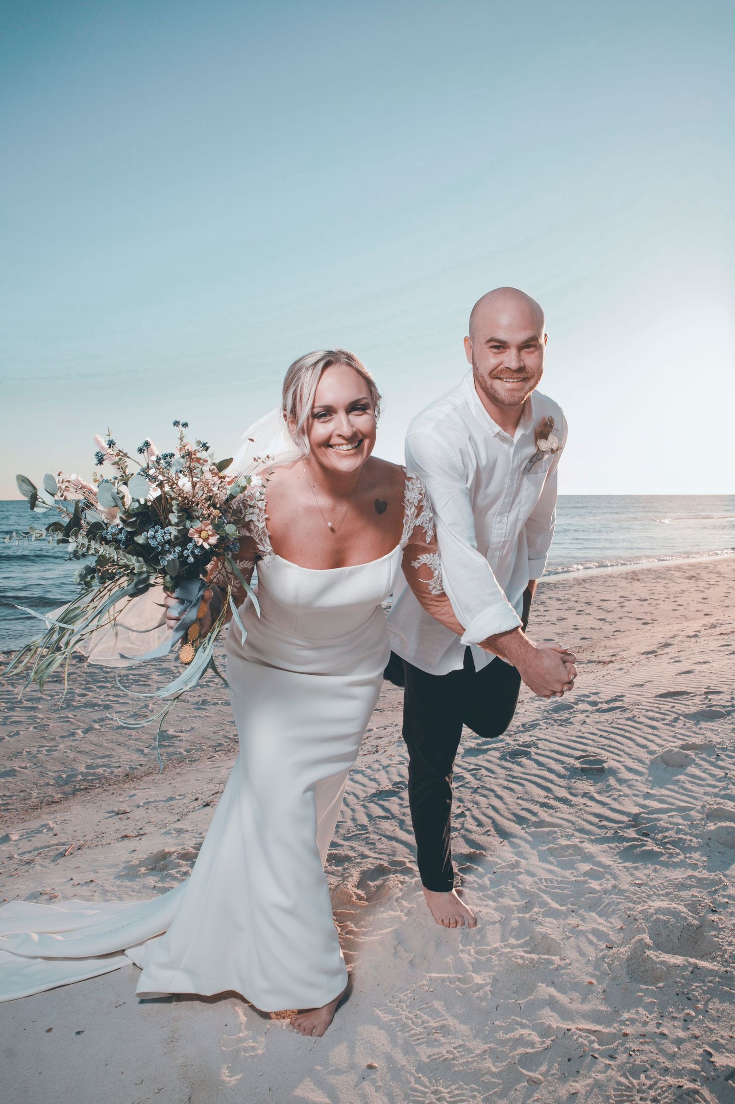 A couple shares joyful moments on a sandy beach during their wedding photoshoot at sunset.