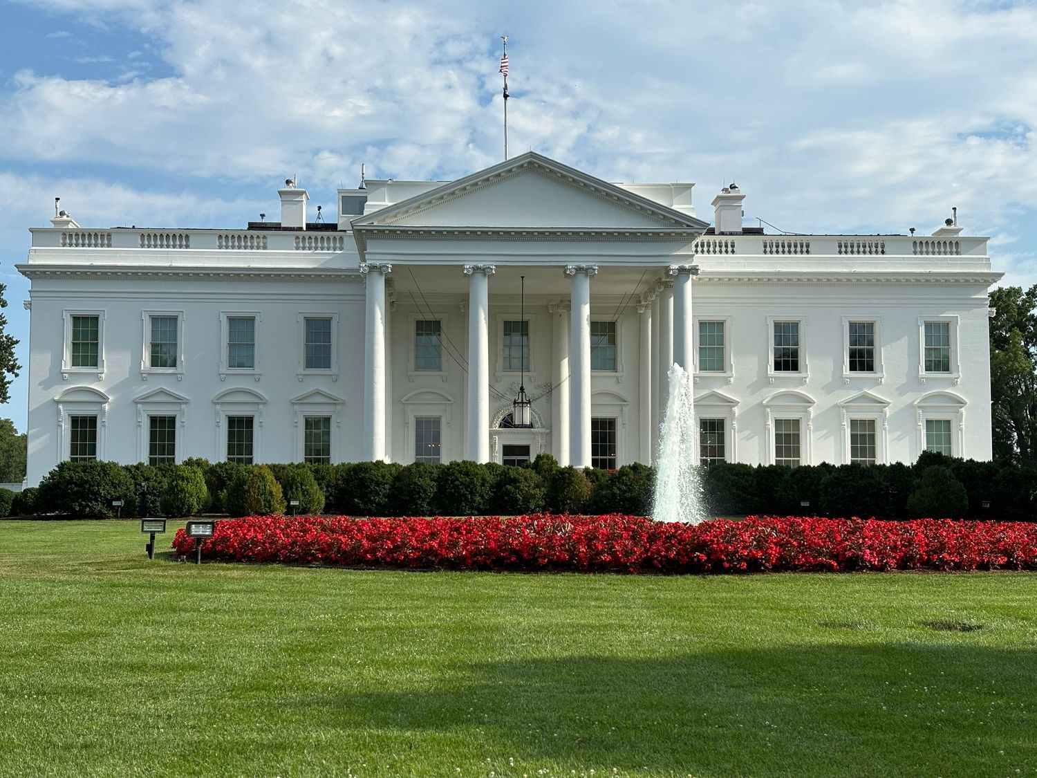 Panoramic view of the White House's iconic south facade with manicured lawn and red flowers in bloom.
