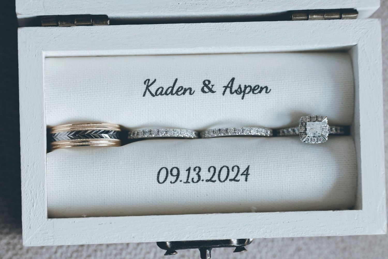 Wedding rings and wedding date displayed in elegant white shadow box frames against a neutral wall.