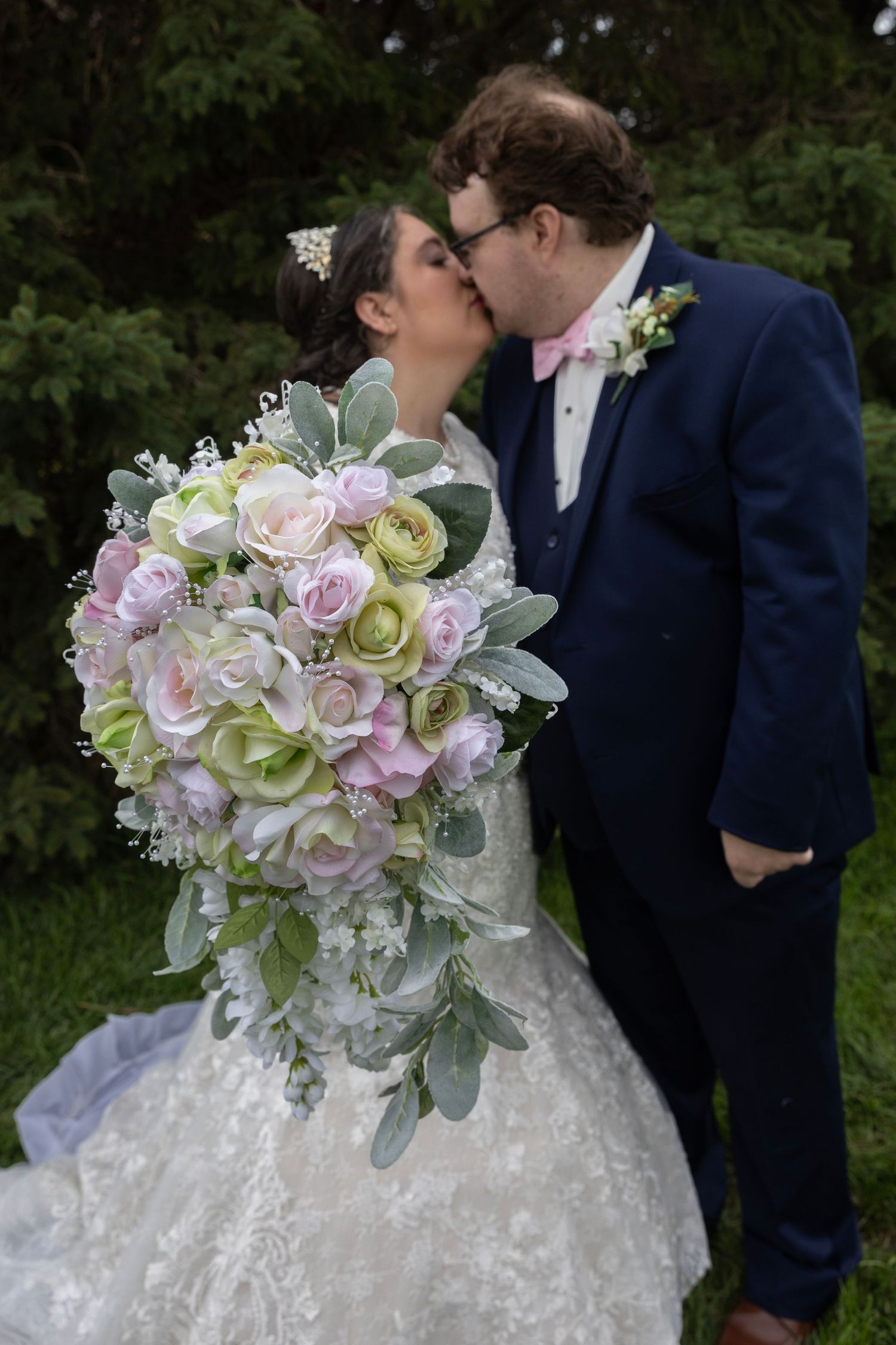 A wedding bouquet of pink and green roses with silvery foliage is prominently displayed against a white lace dress.