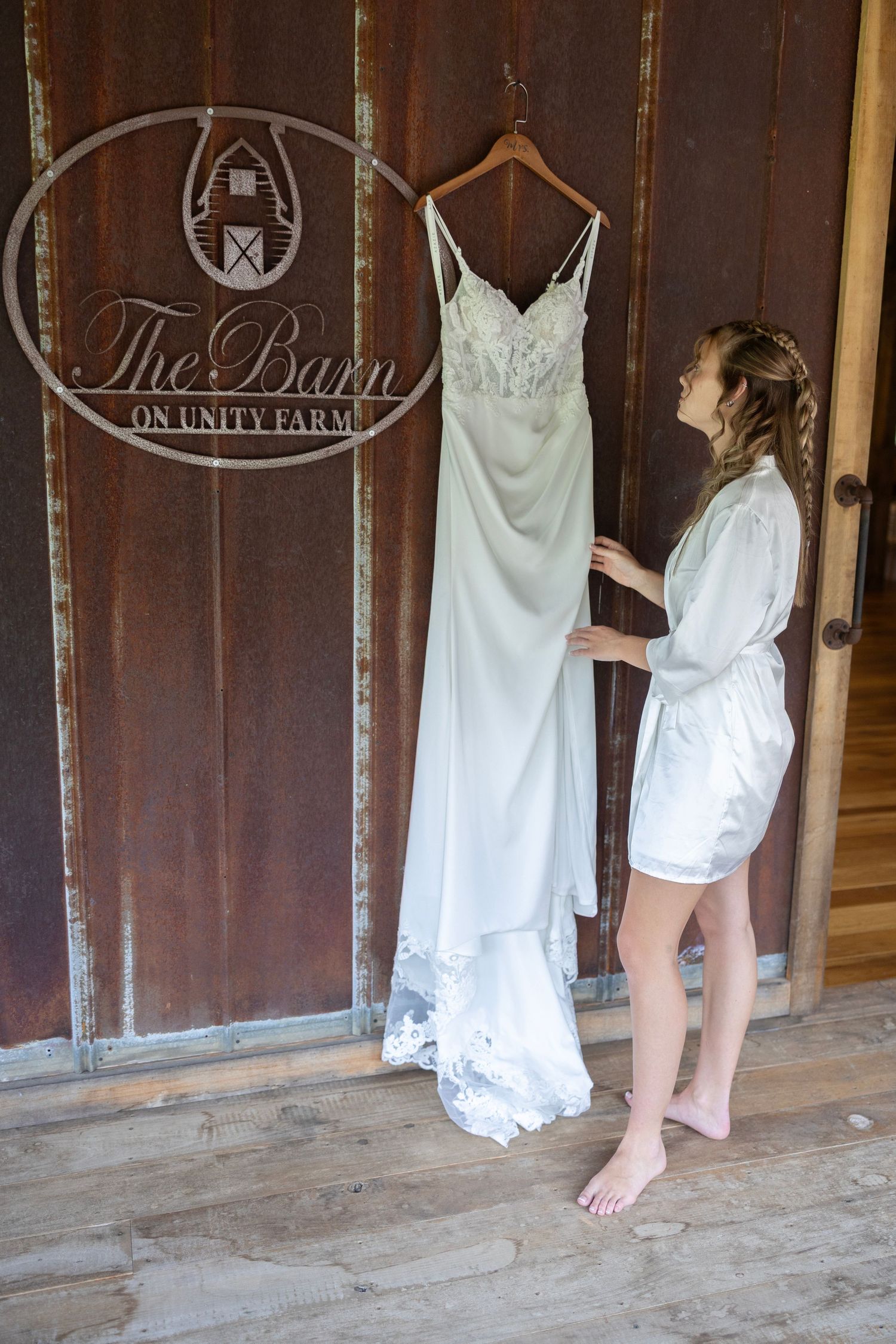 A series of white wedding dresses hanging in a rustic barn venue with wooden doors and decorative logos.