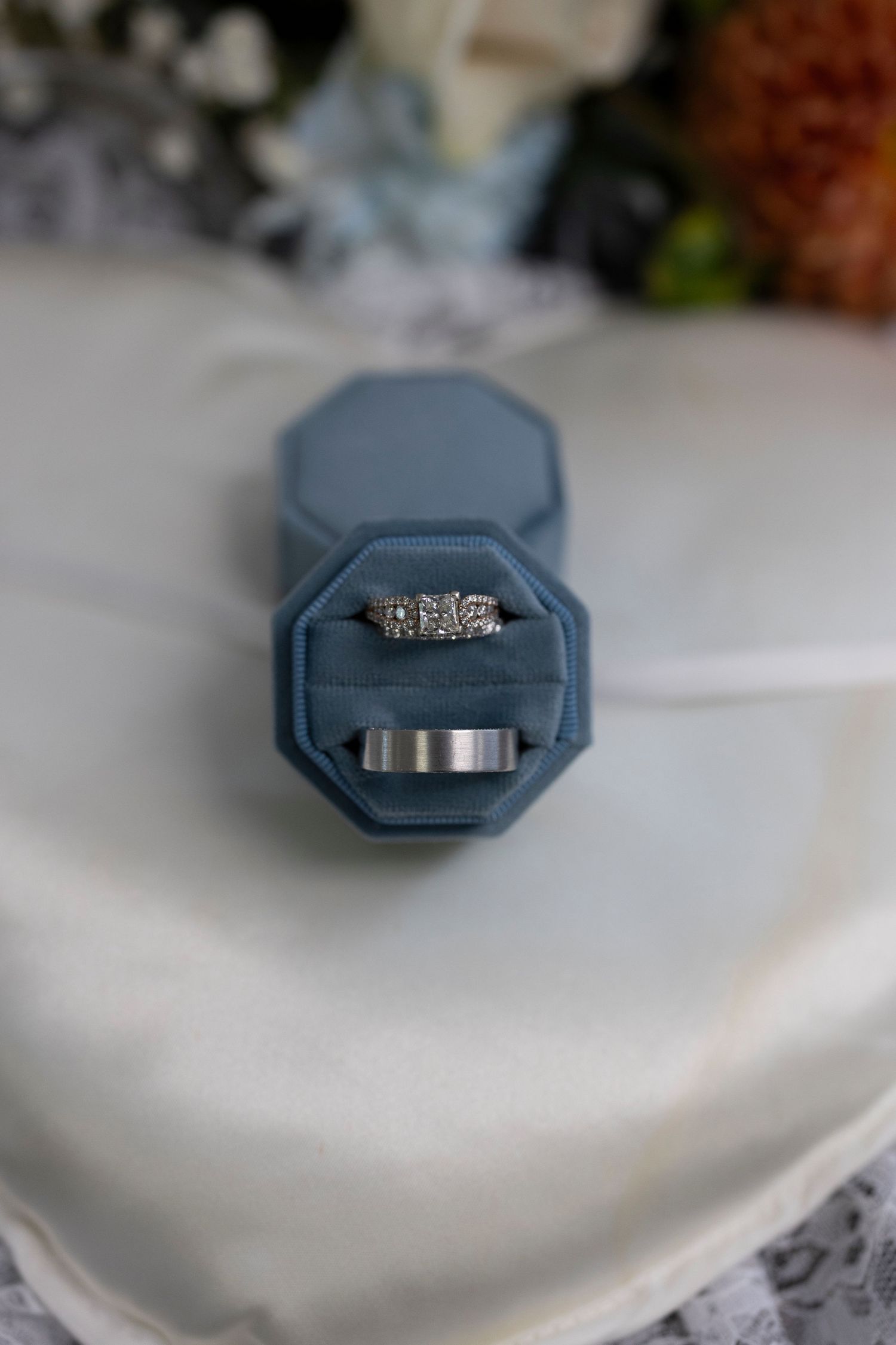 A close-up view of an engagement ring with diamonds in a navy blue ring box on a white surface.