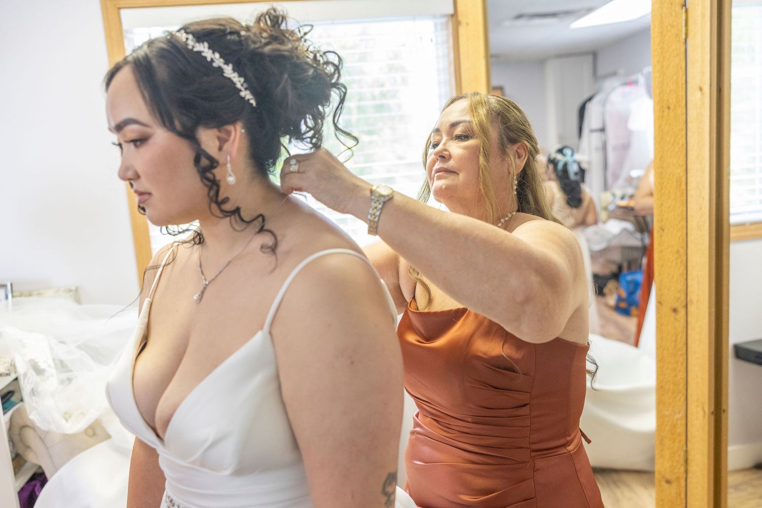 Bridal party gets ready in a bright dressing room with bridesmaids in rust-colored dresses helping with preparations.