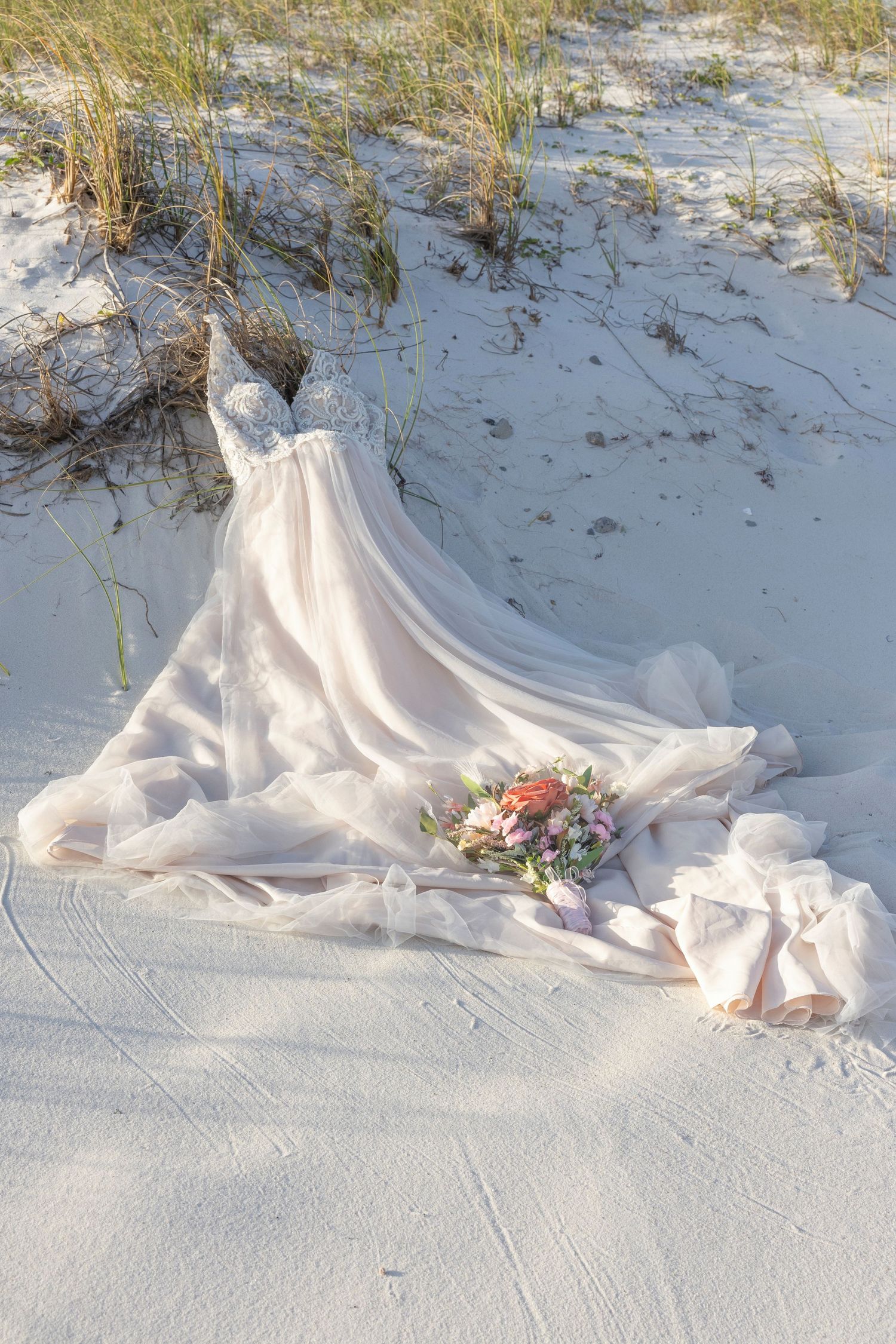 White wedding dress train with floral details elegantly draped across pristine sandy beach at sunset.