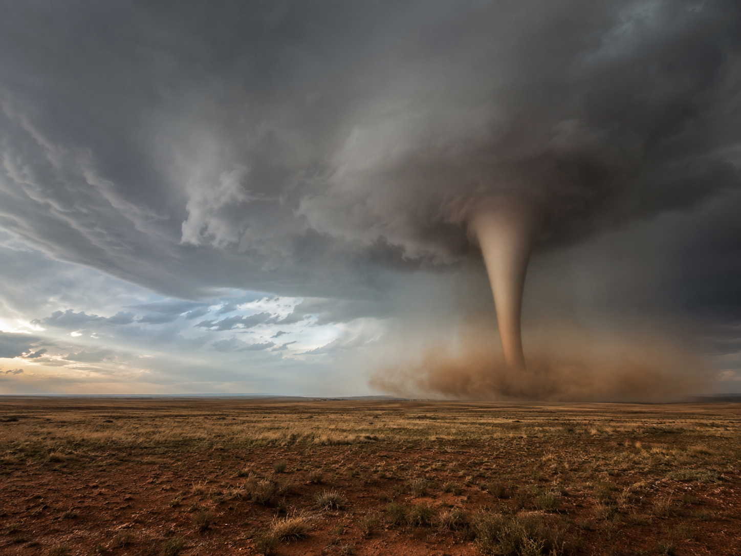 A massive tornado touches down on an arid desert plain under dramatic storm clouds at sunset.