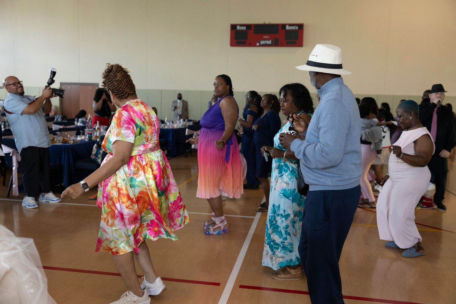 People dancing and socializing at an indoor community event in a gymnasium with festive attire.