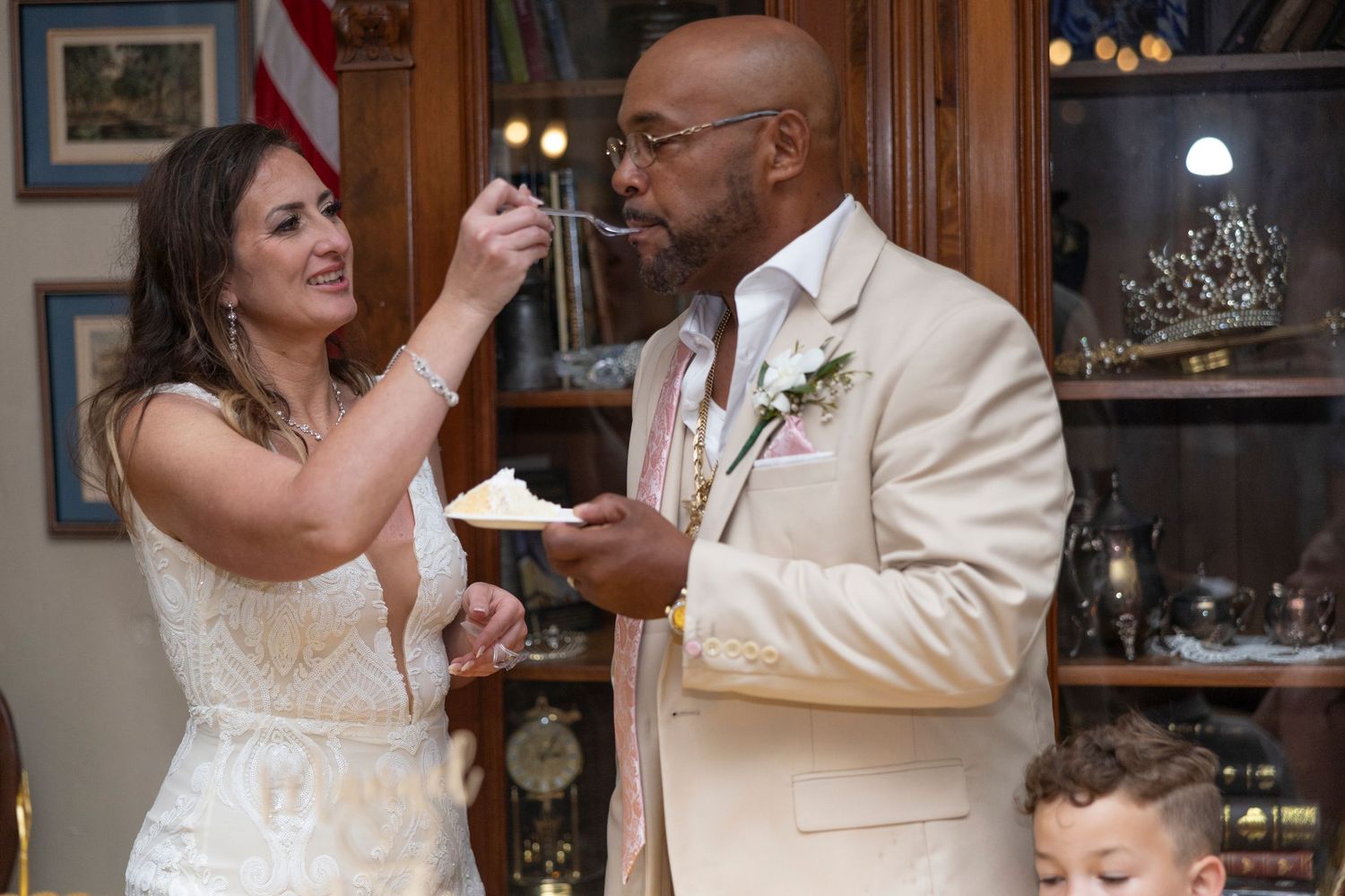 Two wedding guests share a playful moment while eating cake at a reception celebration.