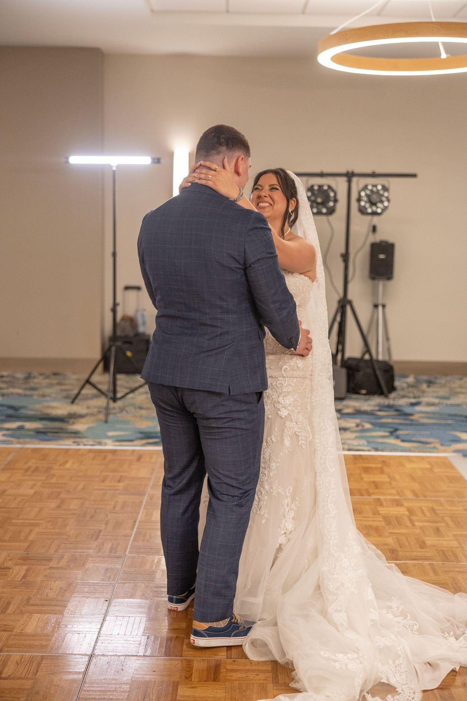 Bride and groom share their first dance in a elegant ballroom, bride smiling in a lace gown with veil.