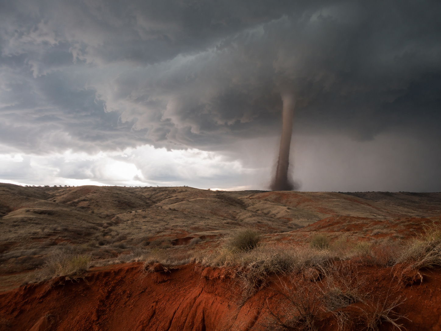 A massive tornado touches down over red desert badlands under dramatic stormy skies.