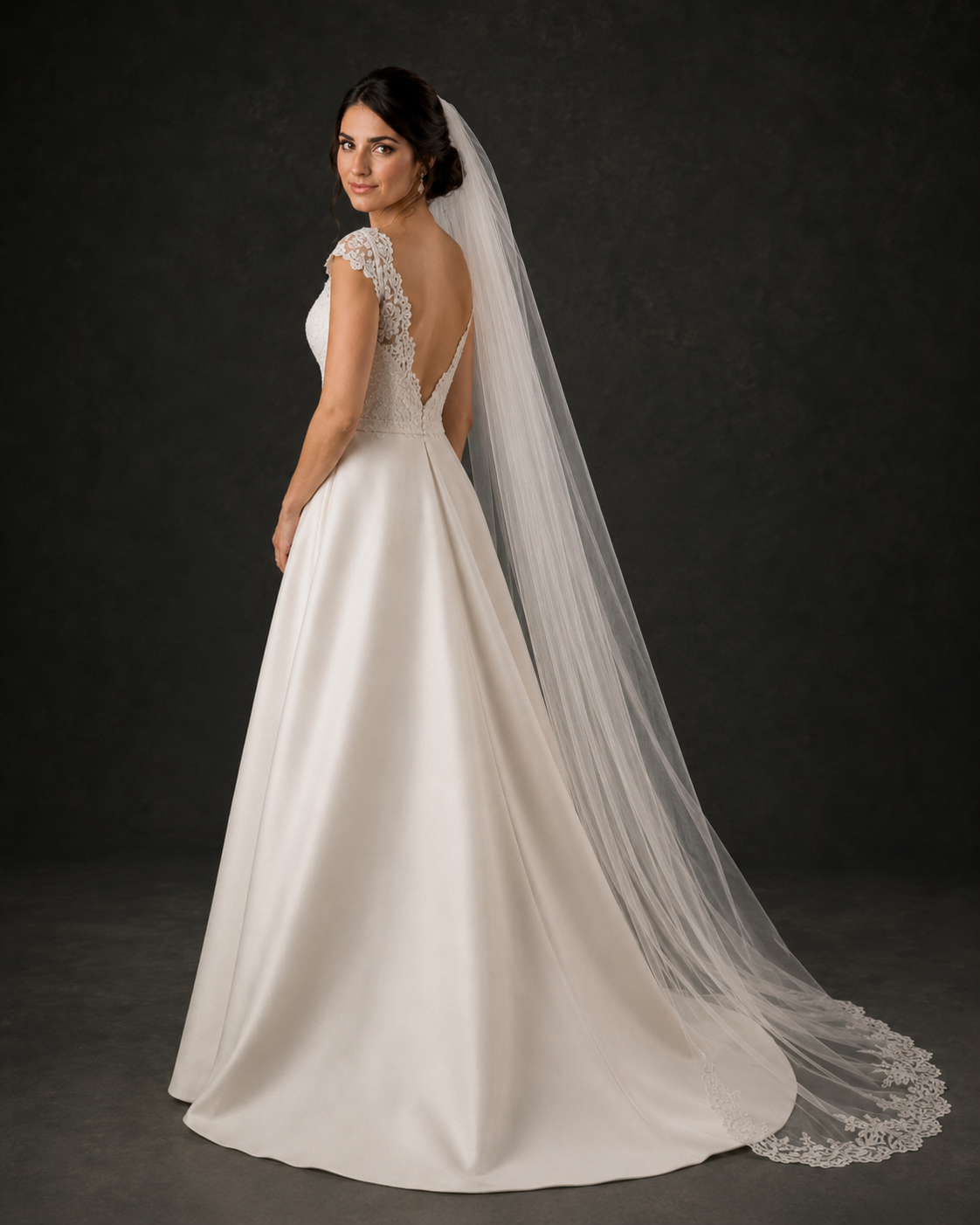 Back view of bride in ivory satin A-line wedding gown with deep V-back and lace-trimmed cathedral veil.