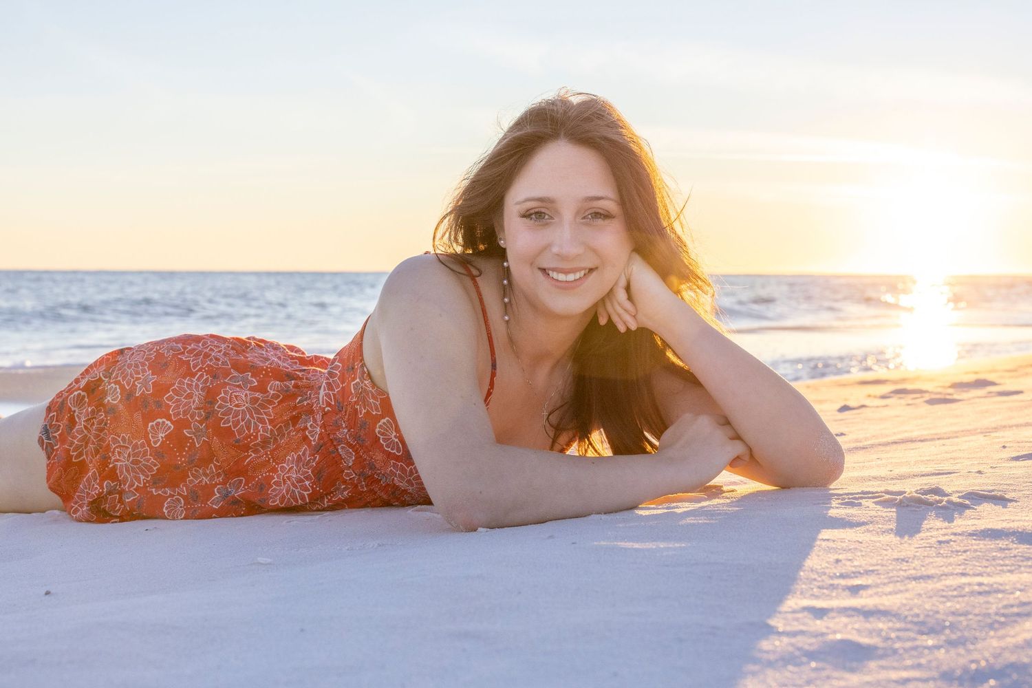 Person lying on sandy beach during golden sunset with waves in background.