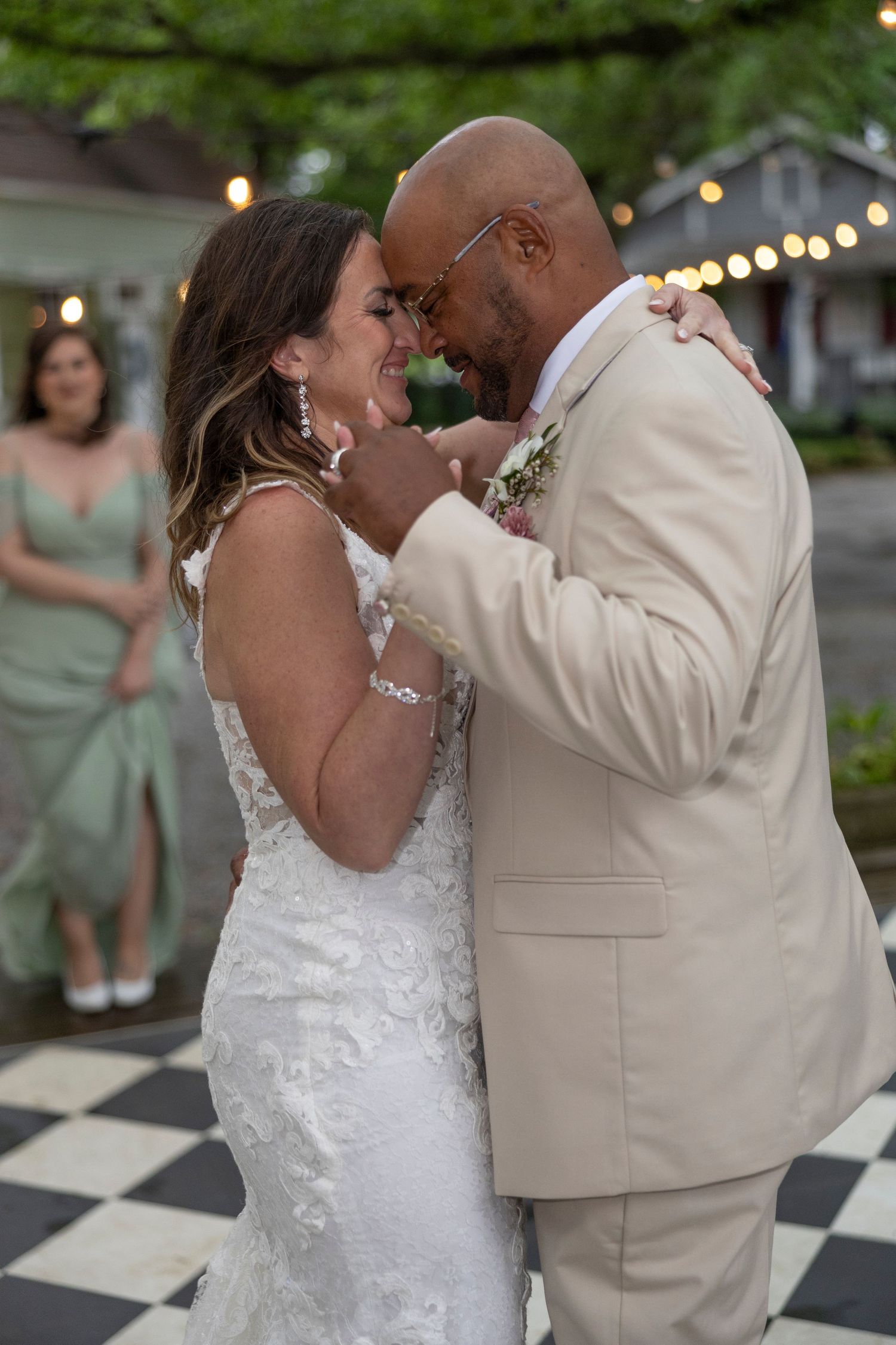 A couple shares their first dance at an outdoor wedding reception on a black and white checkered dance floor.