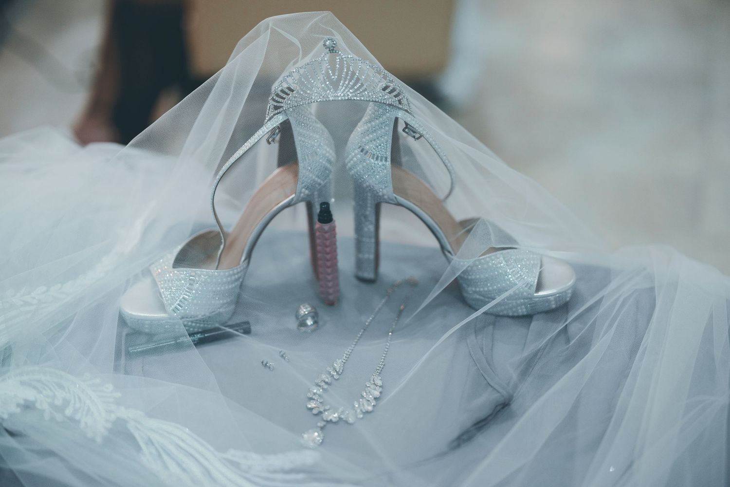 Elegant silver bridal high heels with crystal details rest on delicate white tulle veil.