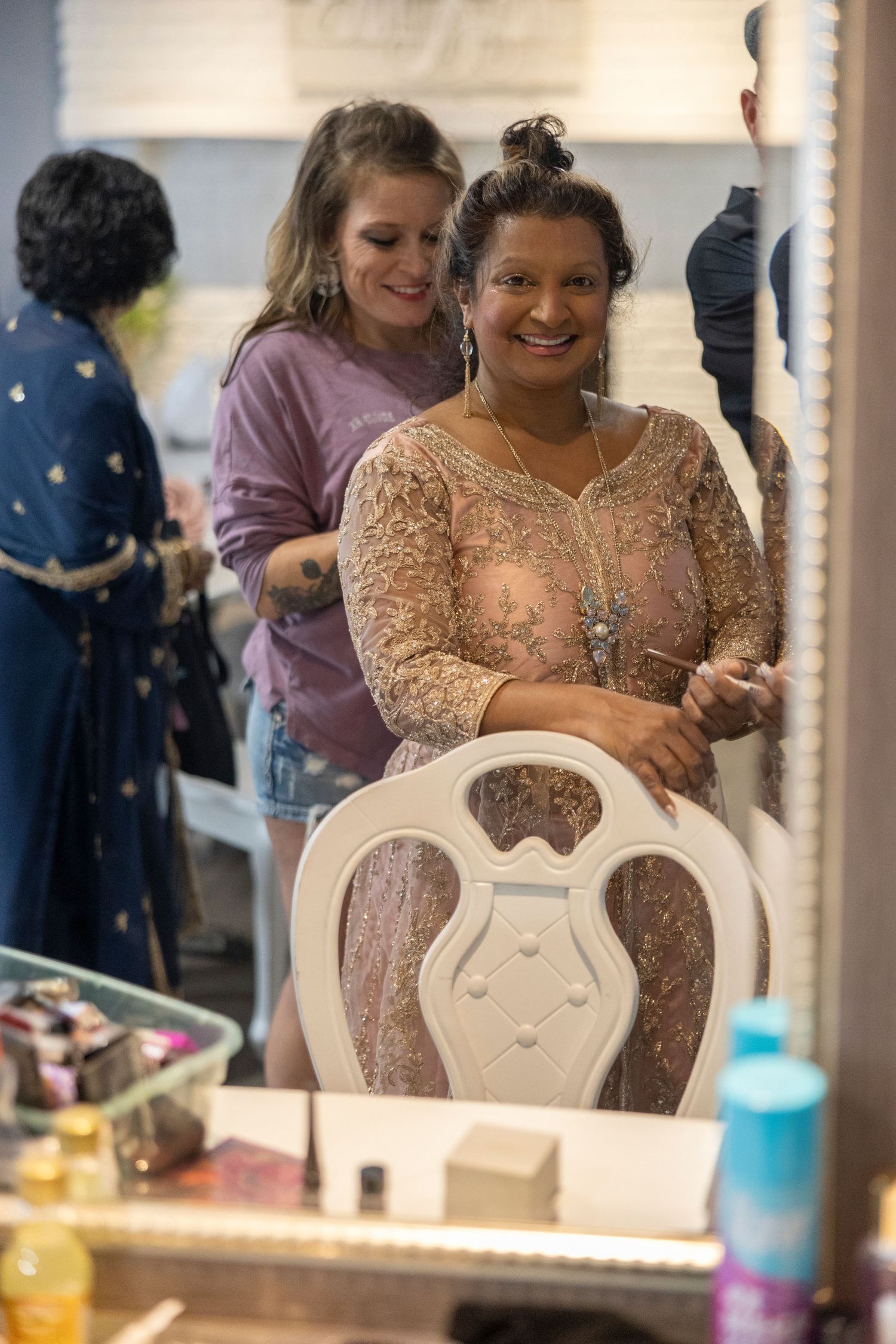 Person wearing a sparkly peach-colored dress sits at a vanity mirror during what appears to be a special occasion.