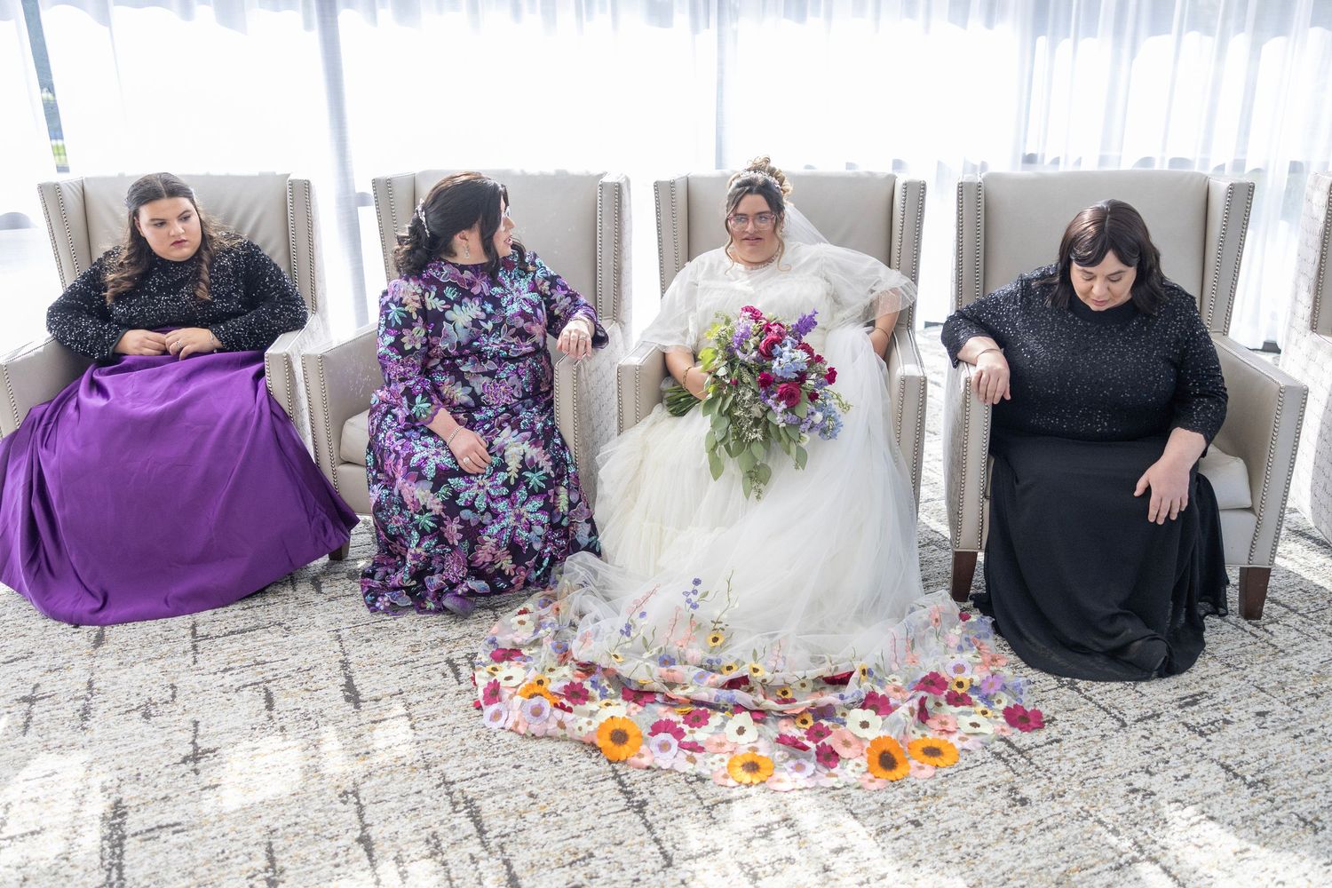 A group of people in formal attire sitting together on white chairs with colorful flower petals scattered on the ground.