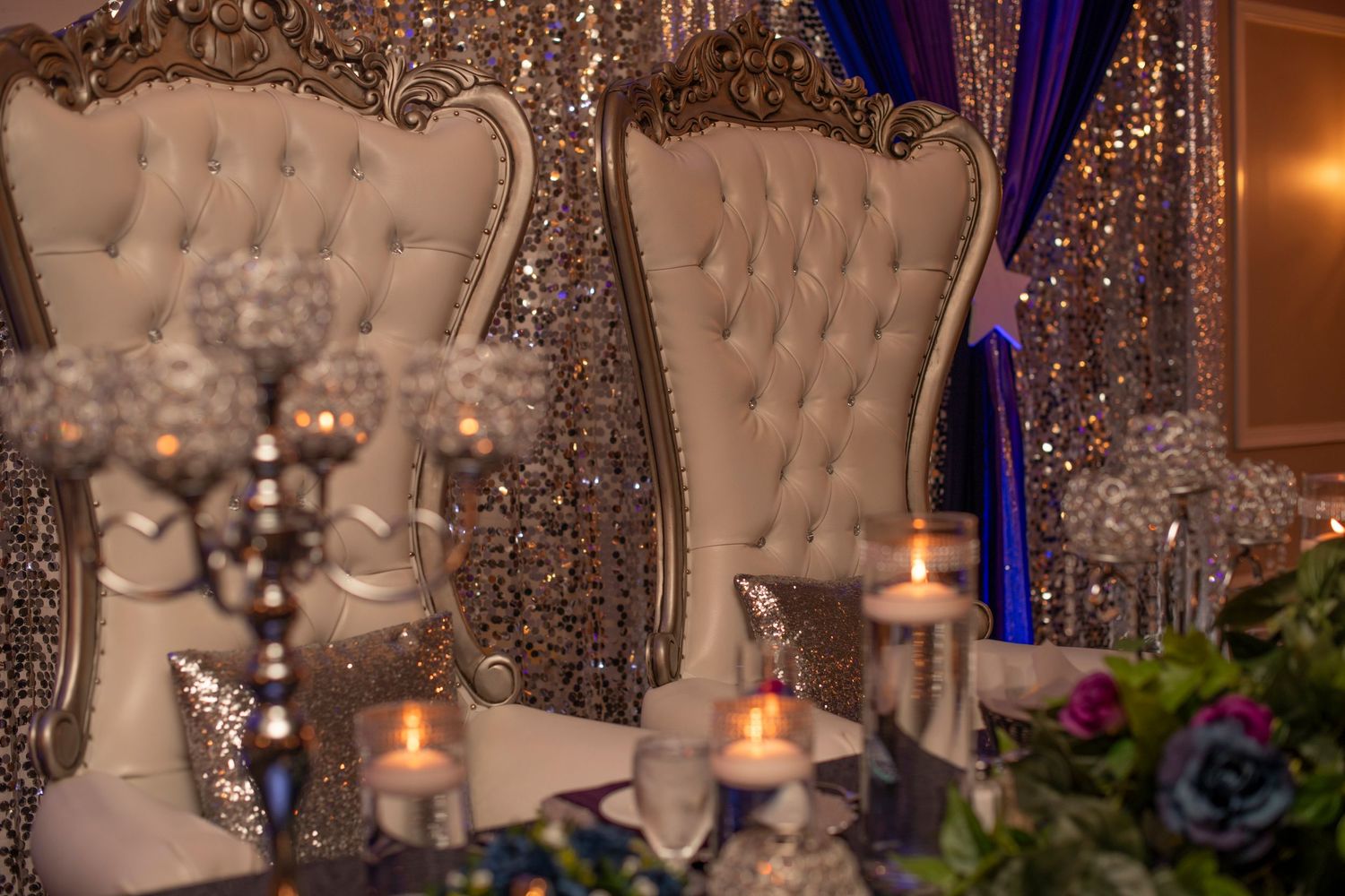 Elegant wedding reception decor featuring tufted high-back chairs, crystal chandeliers, and romantic candlelight.