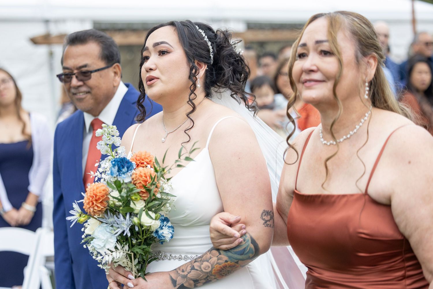 Wedding party poses outdoors with colorful bouquets and rust-colored bridesmaid dresses during summer celebration.