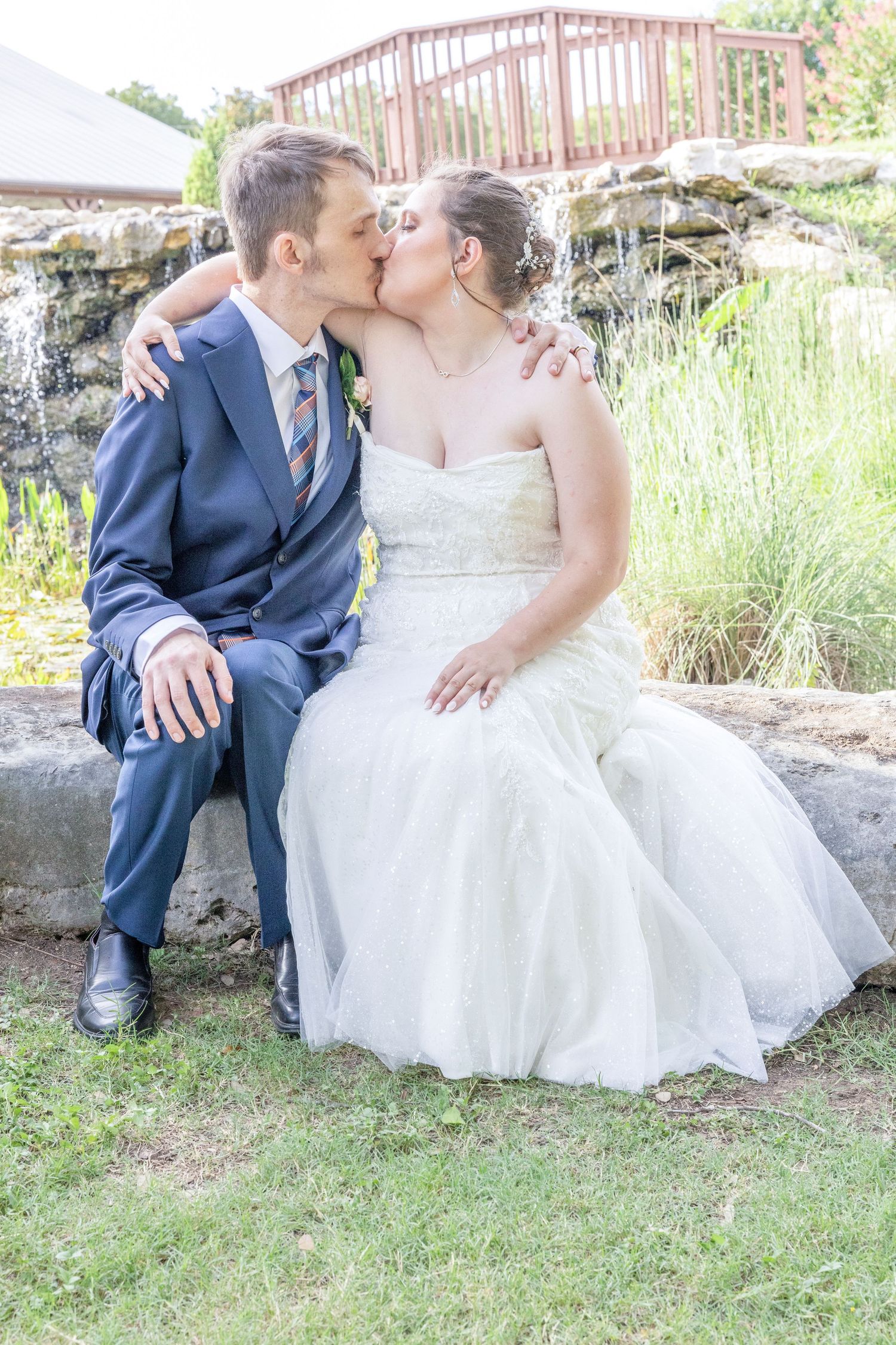 A couple in wedding attire shares an intimate moment while sitting on stone steps surrounded by greenery.