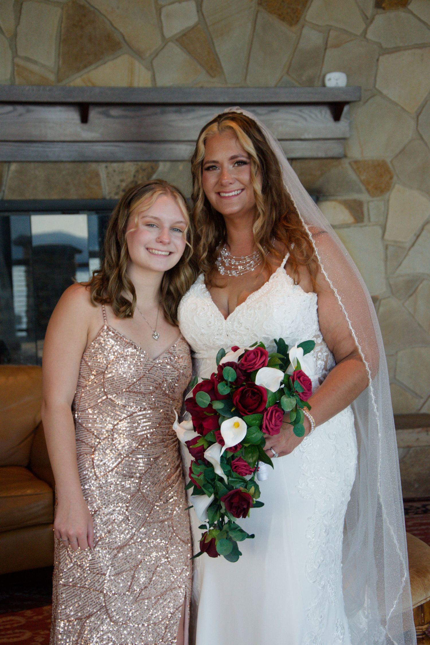 Bride in white lace gown and bridesmaid in champagne sequin dress pose with burgundy and white rose bouquets.