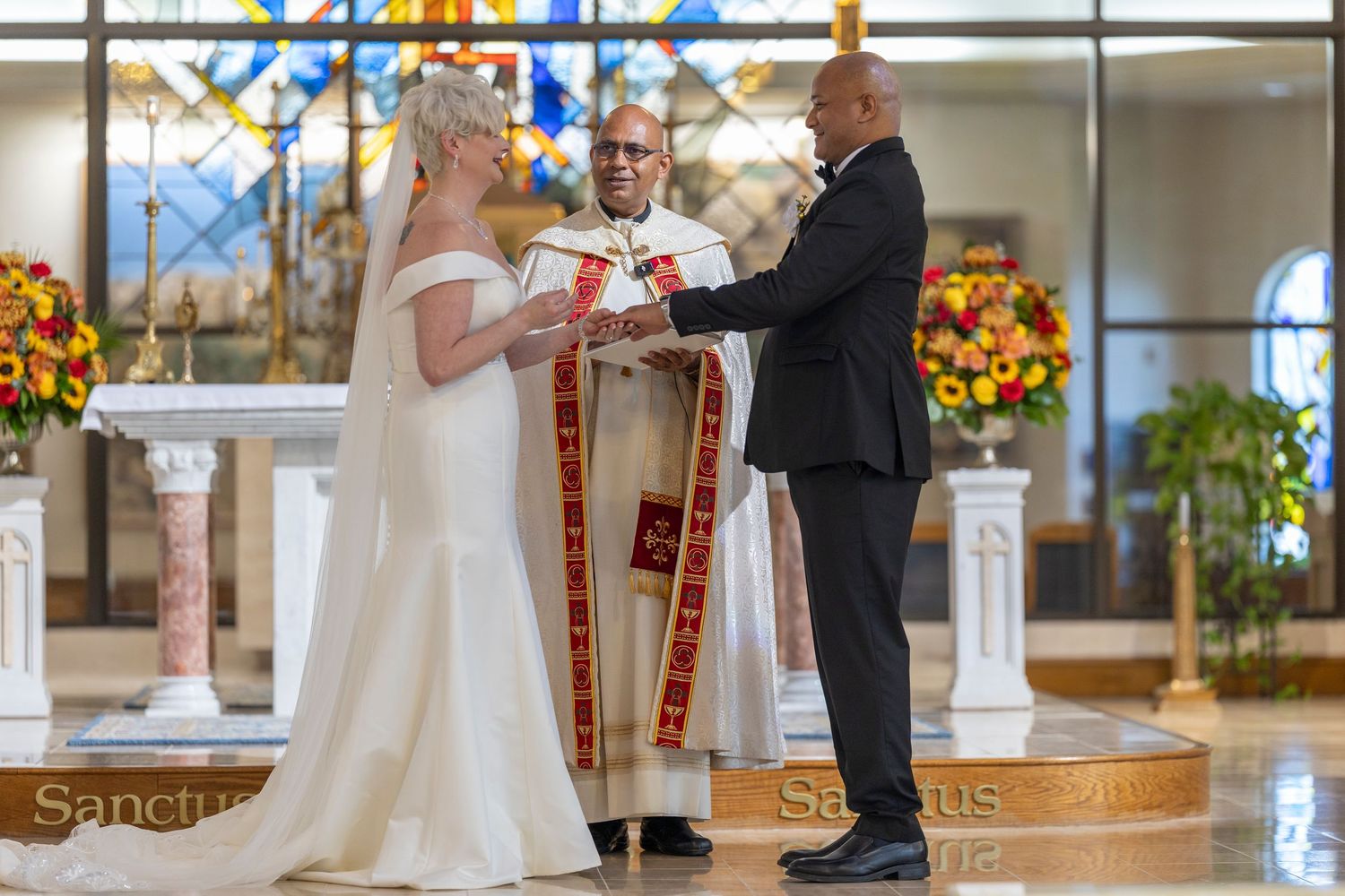 A wedding ceremony takes place in an elegant church with white columns and autumn floral decorations.