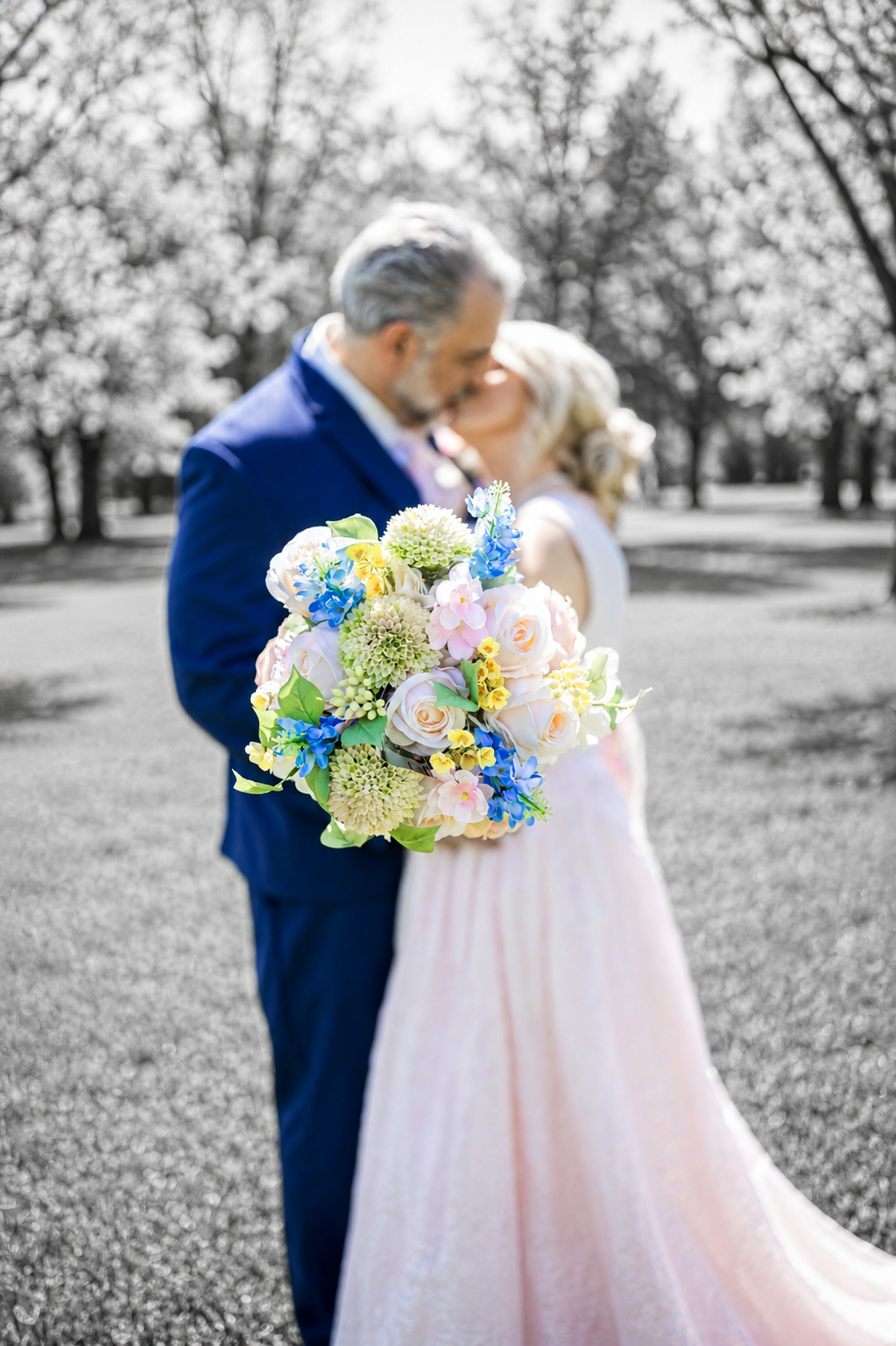 Couple kissing at wedding with colorful bridal bouquet of roses and blue flowers.