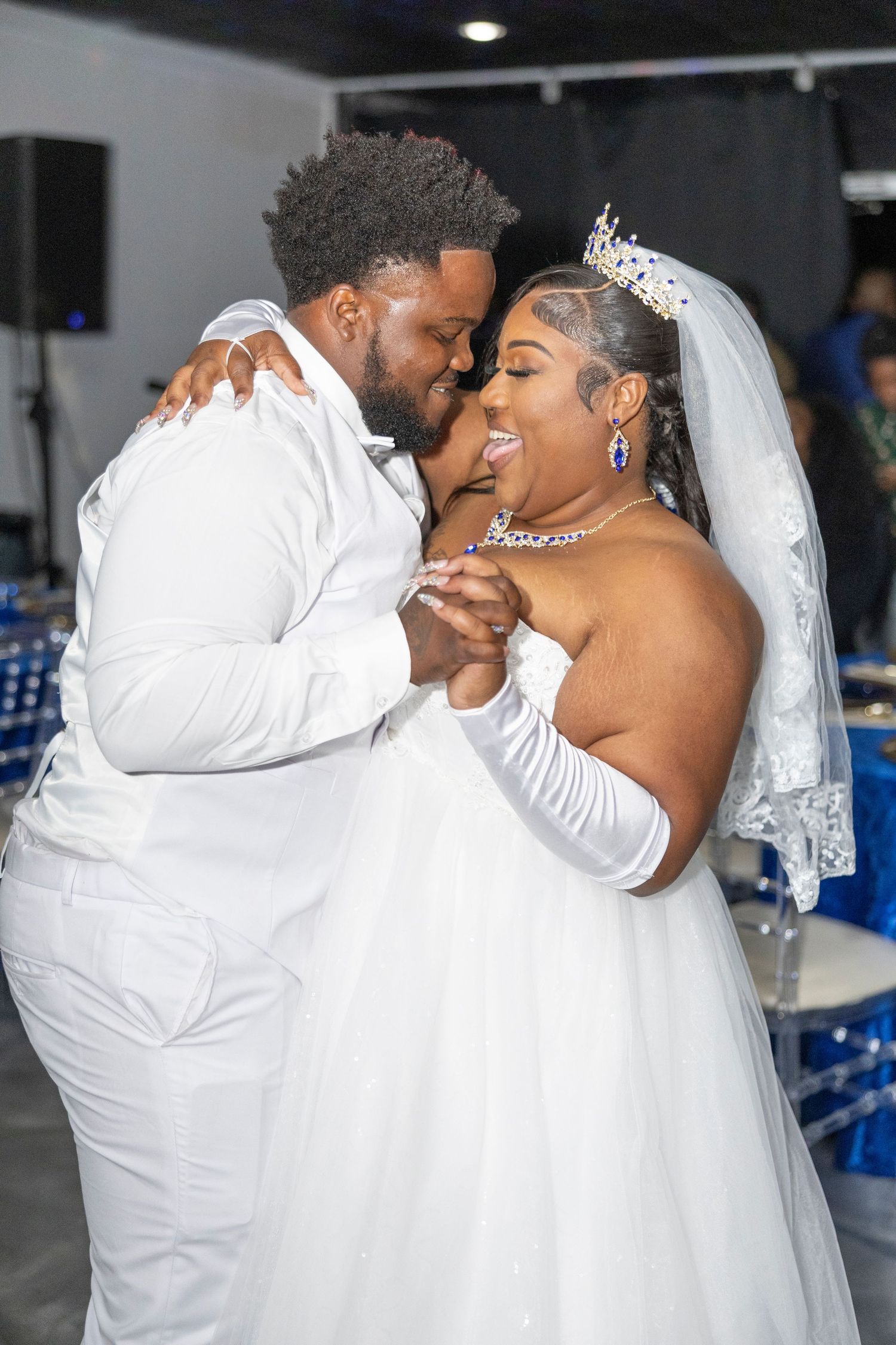A joyful bride and groom share their first dance in white wedding attire at a decorated reception venue.