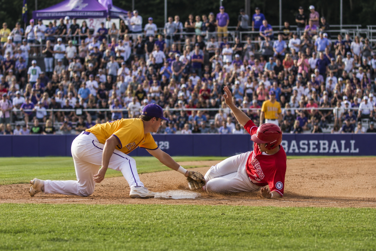 Baseball player in yellow uniform tags out sliding runner in red during a competitive game.